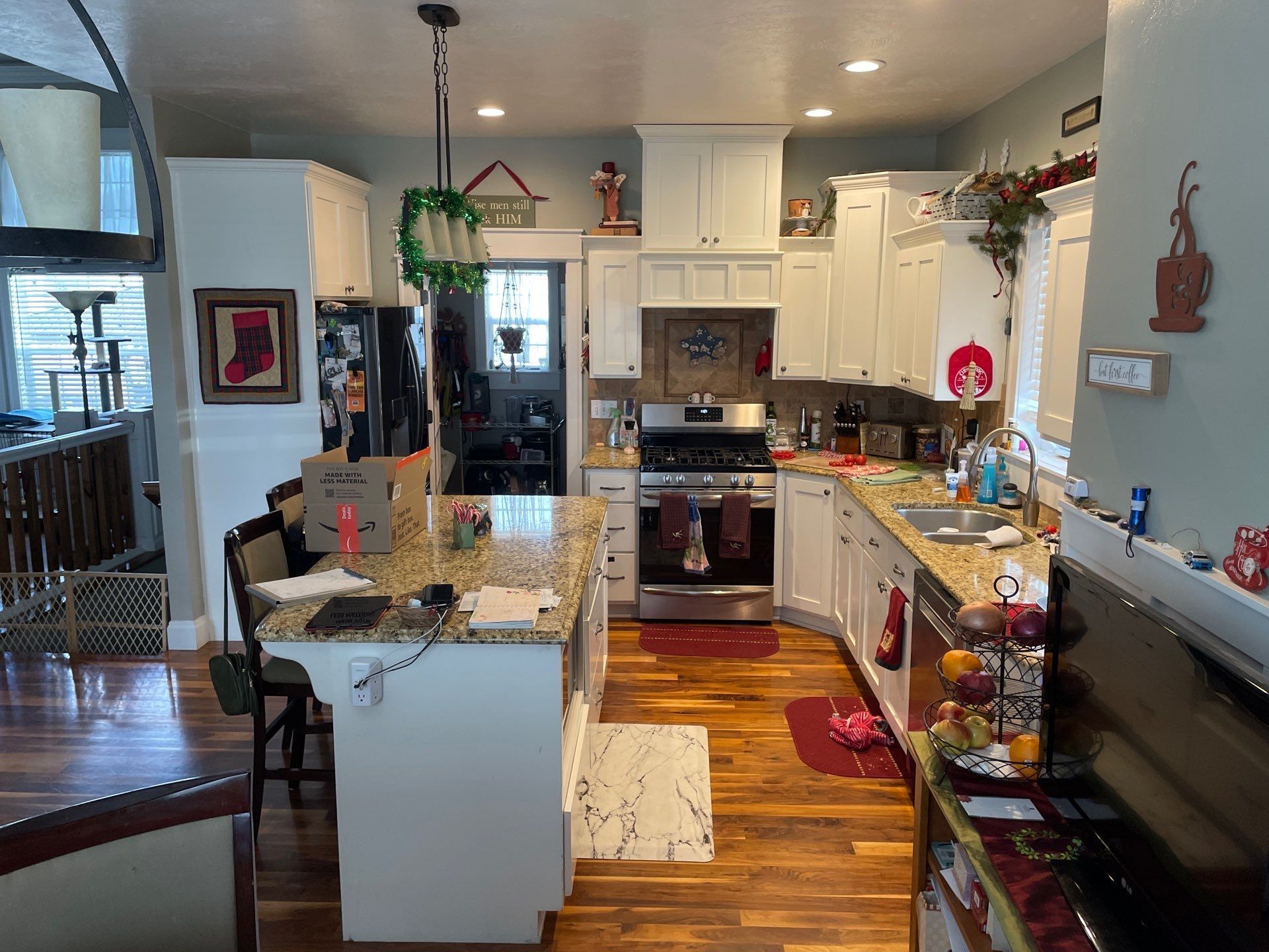 Bright kitchen with granite island, white cabinets, hardwood floor, and hanging plants under ceiling lights