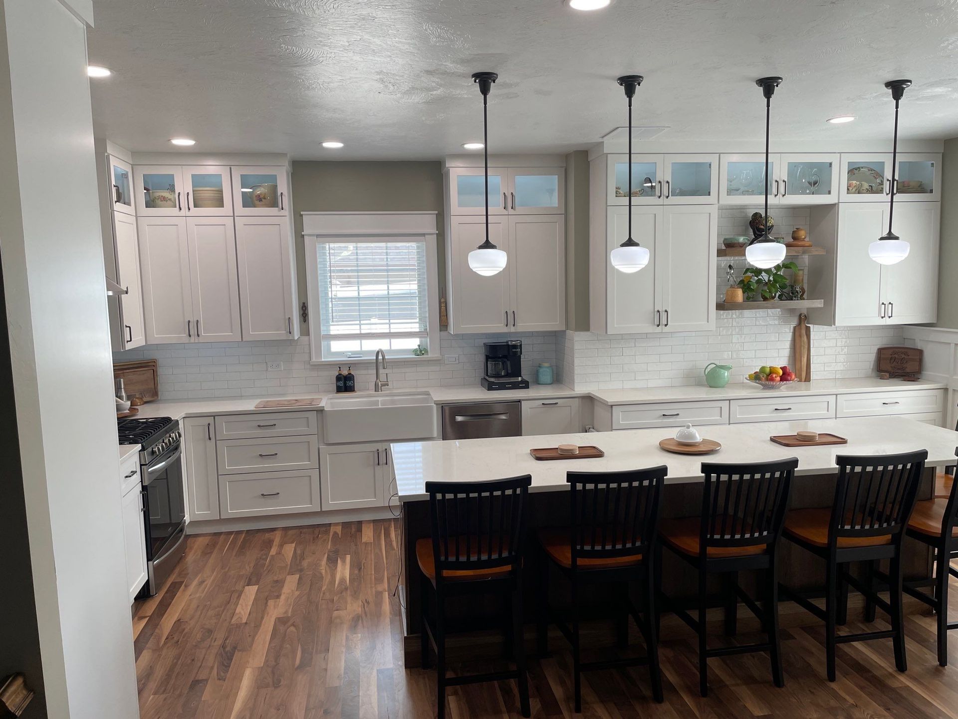 Bright modern kitchen with white cabinets, island seating, pendant lights, and wood floors