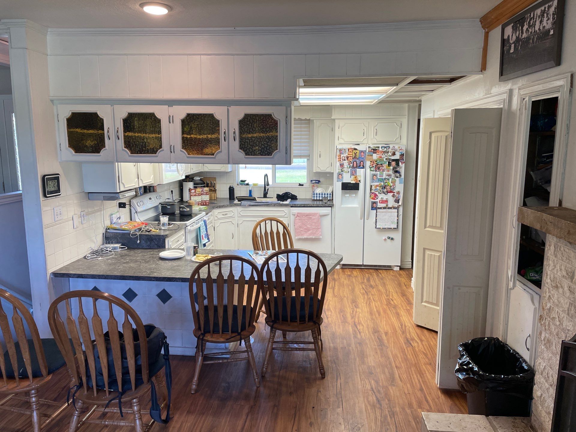 Bright kitchen with white cabinets, wood floor, island, dining chairs, and refrigerator covered in magnets