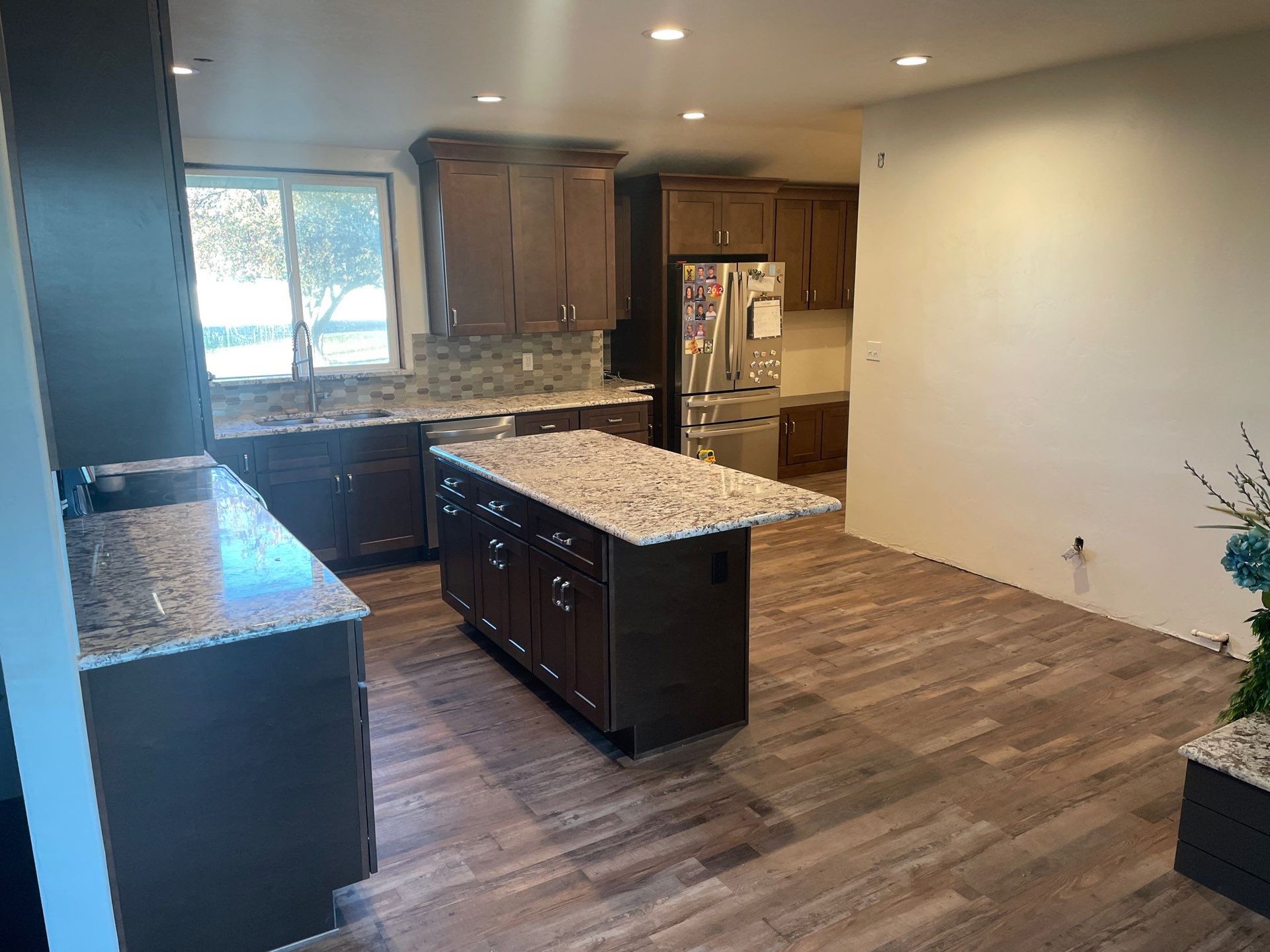 Modern open-concept kitchen with granite island, dark cabinets, and wood-look flooring