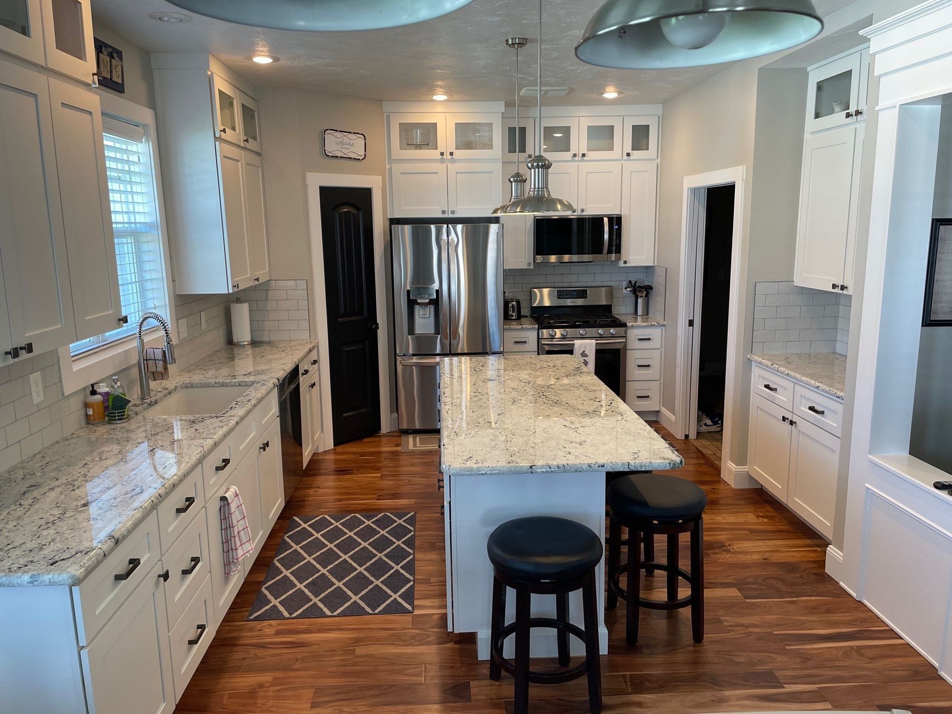Bright, modern kitchen with white cabinets, granite island, stainless steel appliances, and two dark stools.