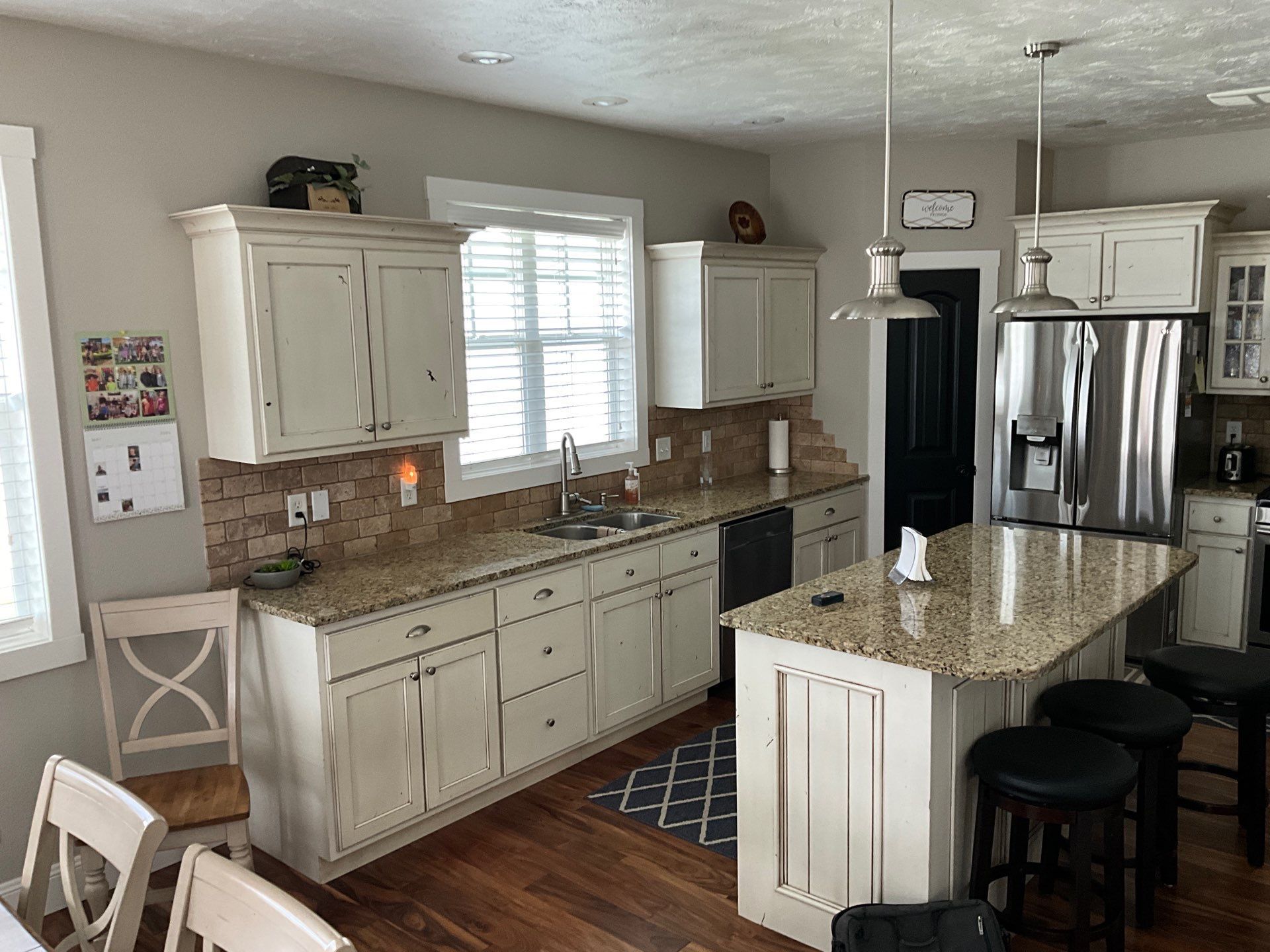 Bright kitchen with white cabinets, granite island, stainless fridge, and stools by the counter