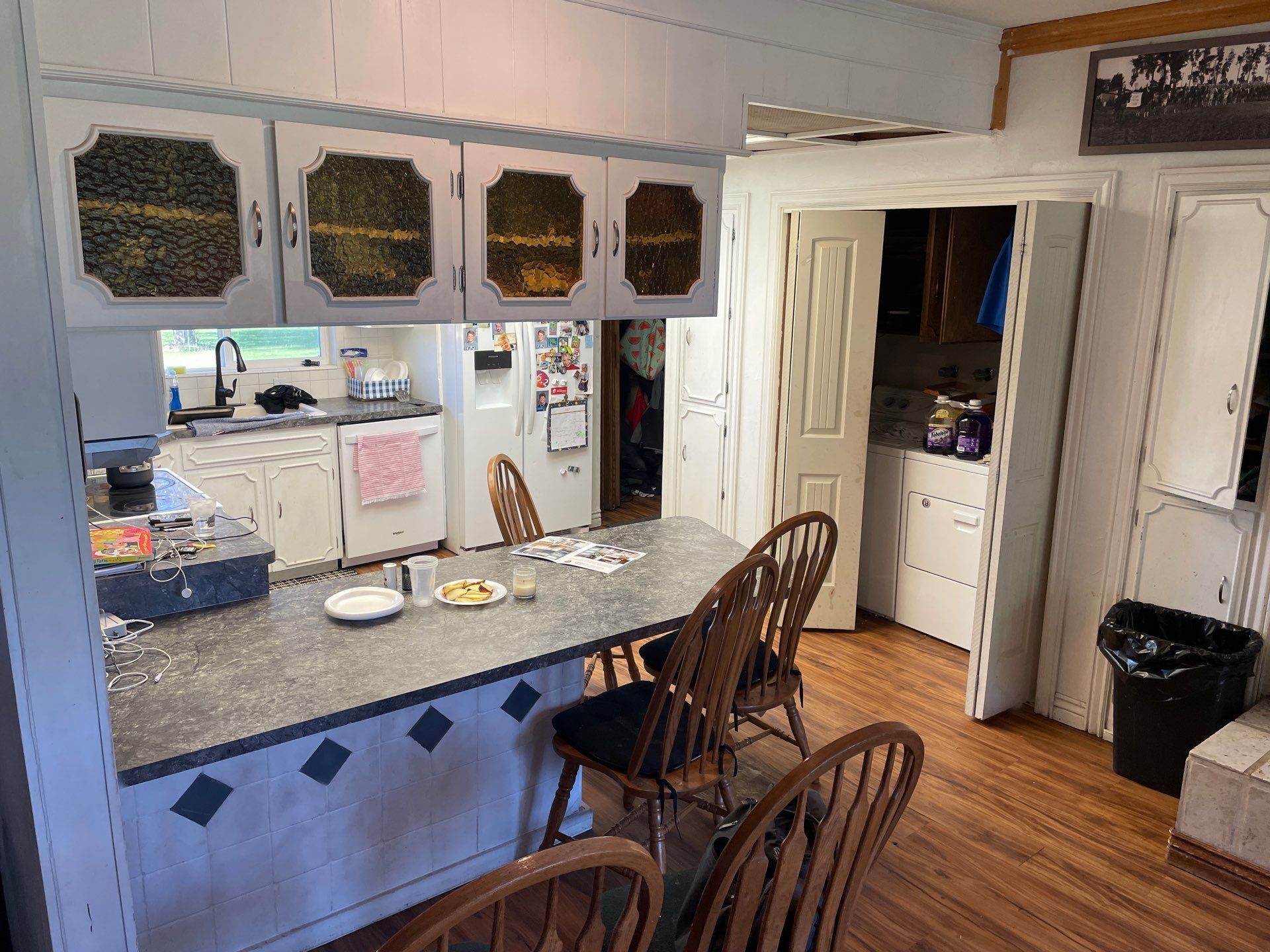 Small kitchen with a wide pass-through counter, white cabinets, and two wooden chairs on a wood floor.
