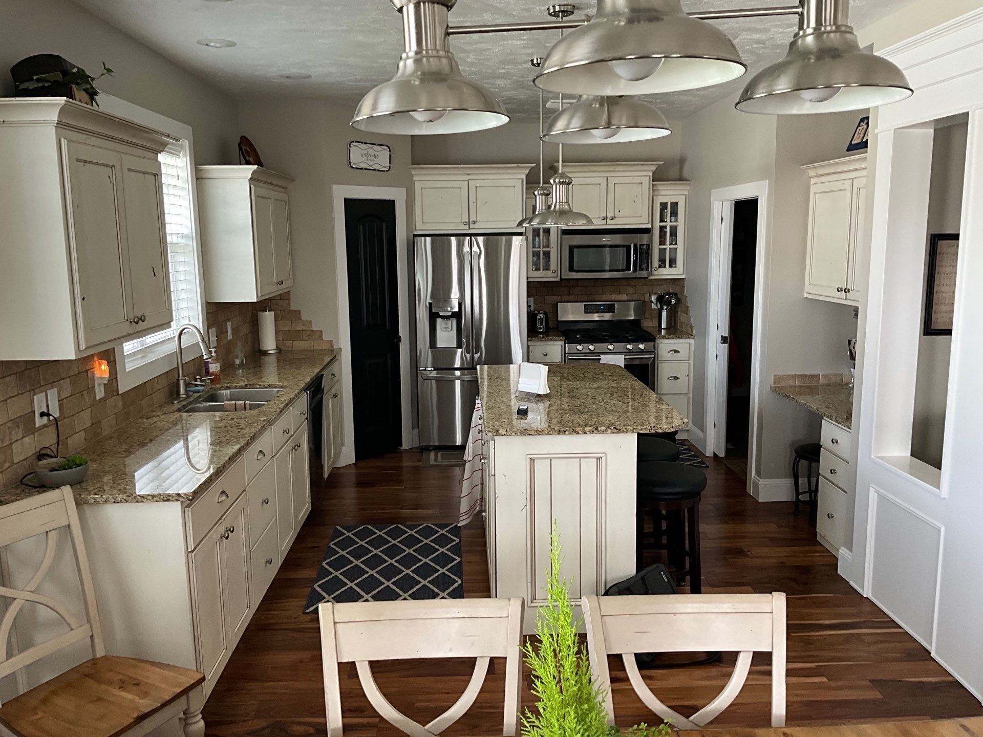 Bright kitchen with granite island, stainless appliances, pendant lights, and wood floors.