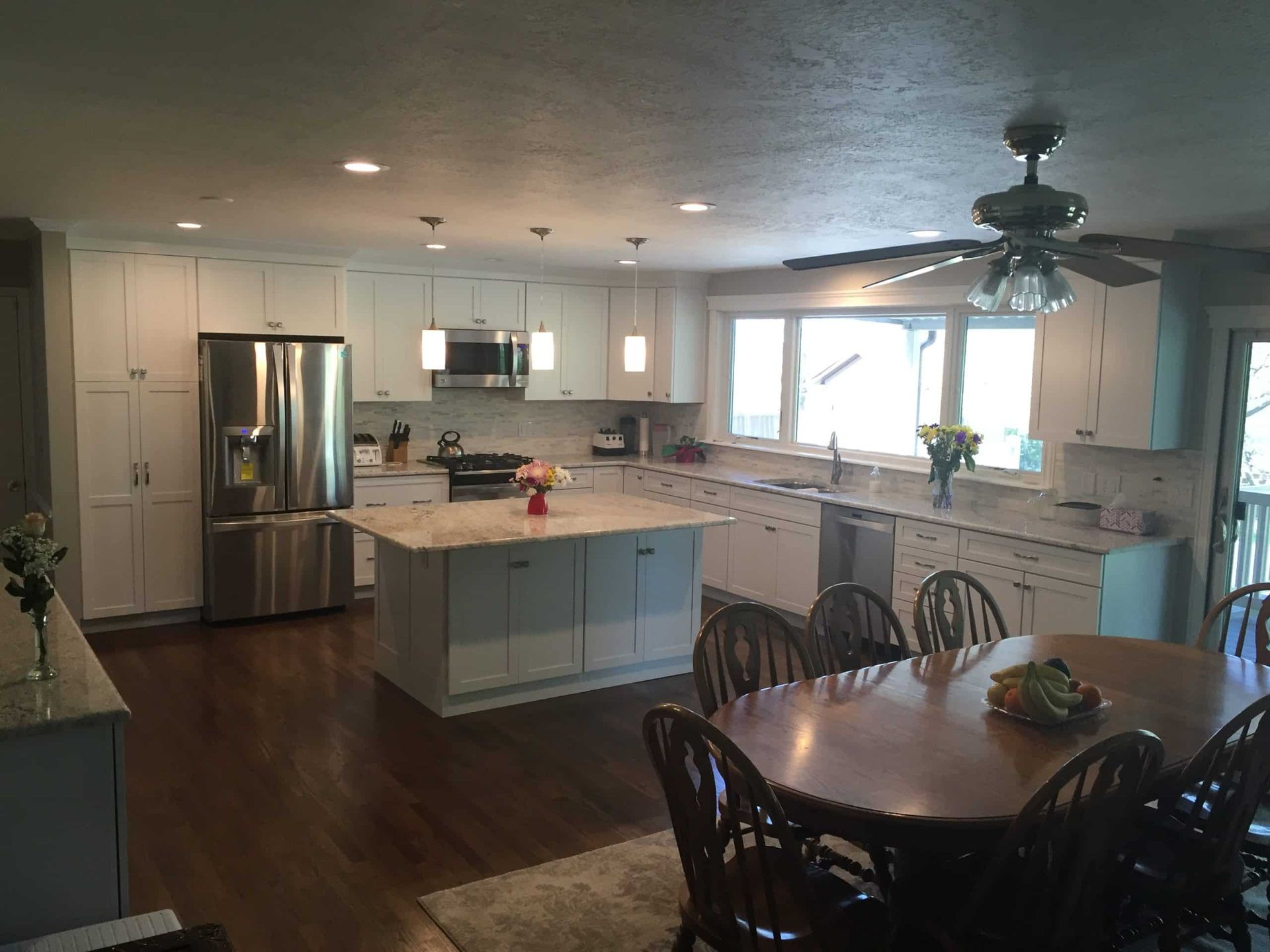 Bright kitchen and dining area with white cabinets, island, stainless fridge, and dark wood table with chairs.