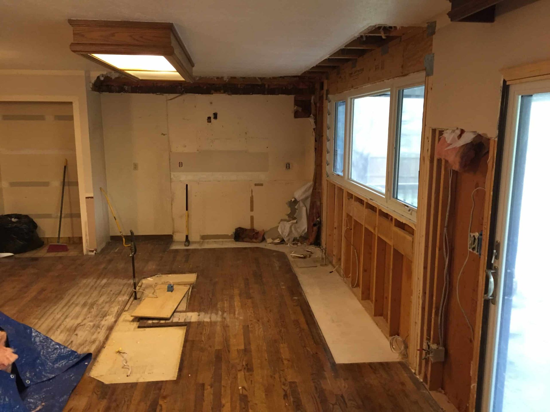 Partially demolished room with exposed studs, scattered flooring, and daylight through windows