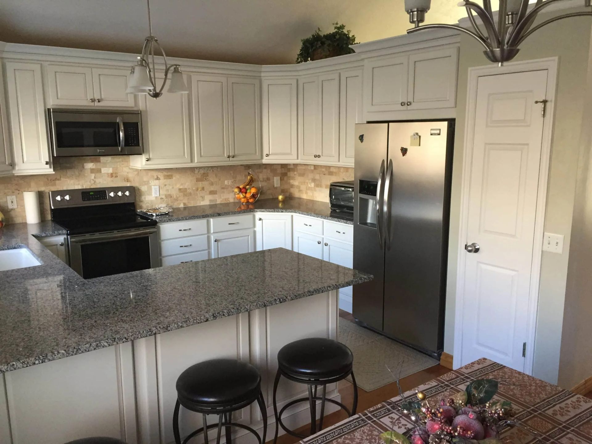 Bright kitchen with white cabinets, stainless appliances, granite island, and two black stools