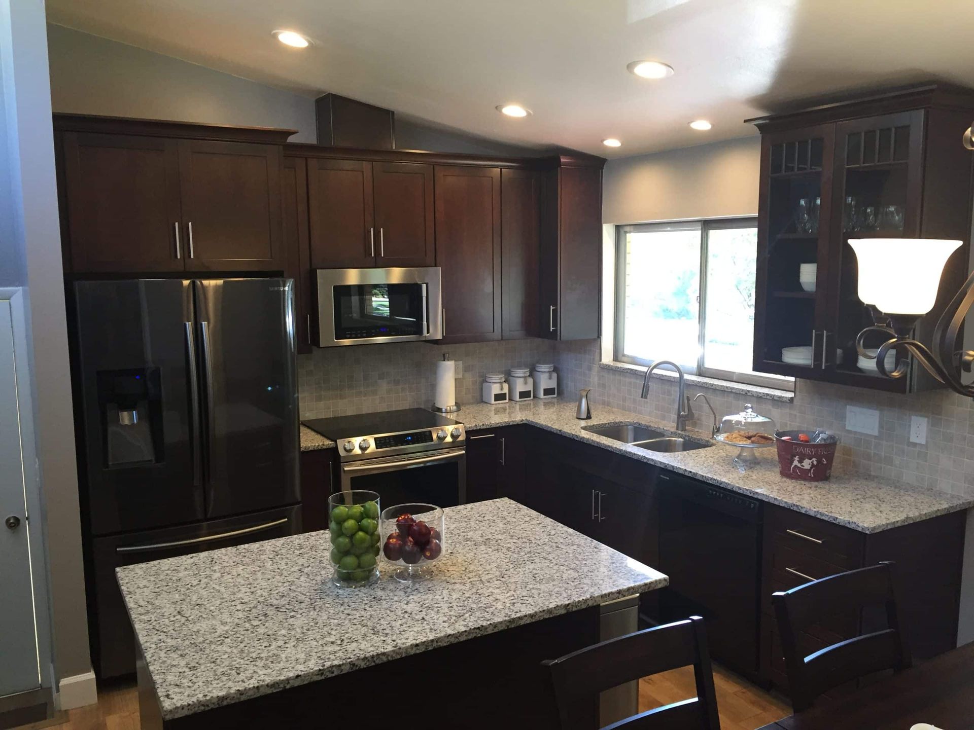 Modern kitchen with dark wood cabinets, granite island, stainless appliances, and a window over the sink.