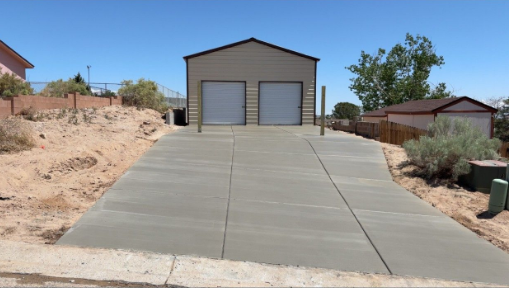 Concrete driveway leading to a two-bay garage with metal doors and a brown exterior. Blue sky in the background.