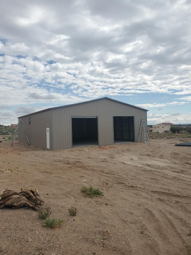 Gray metal building with two garage doors, in a desert setting under a cloudy sky.