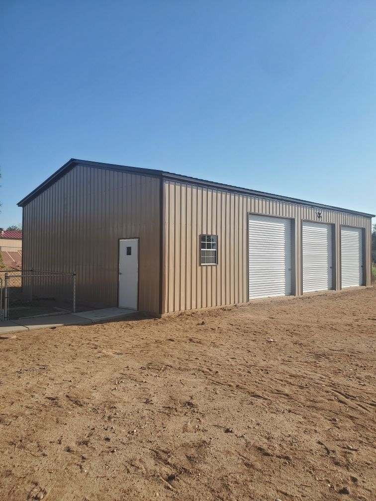 Tan metal building with three garage doors, a door, and a window; on dirt ground.