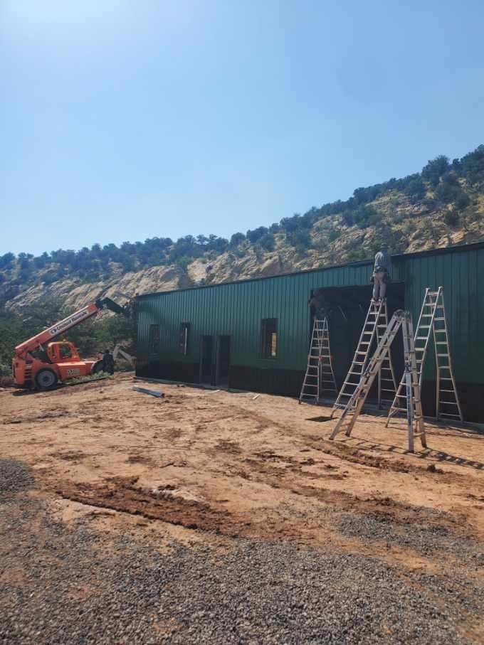 Construction workers on ladders and a lift work on a green building in a hillside setting.