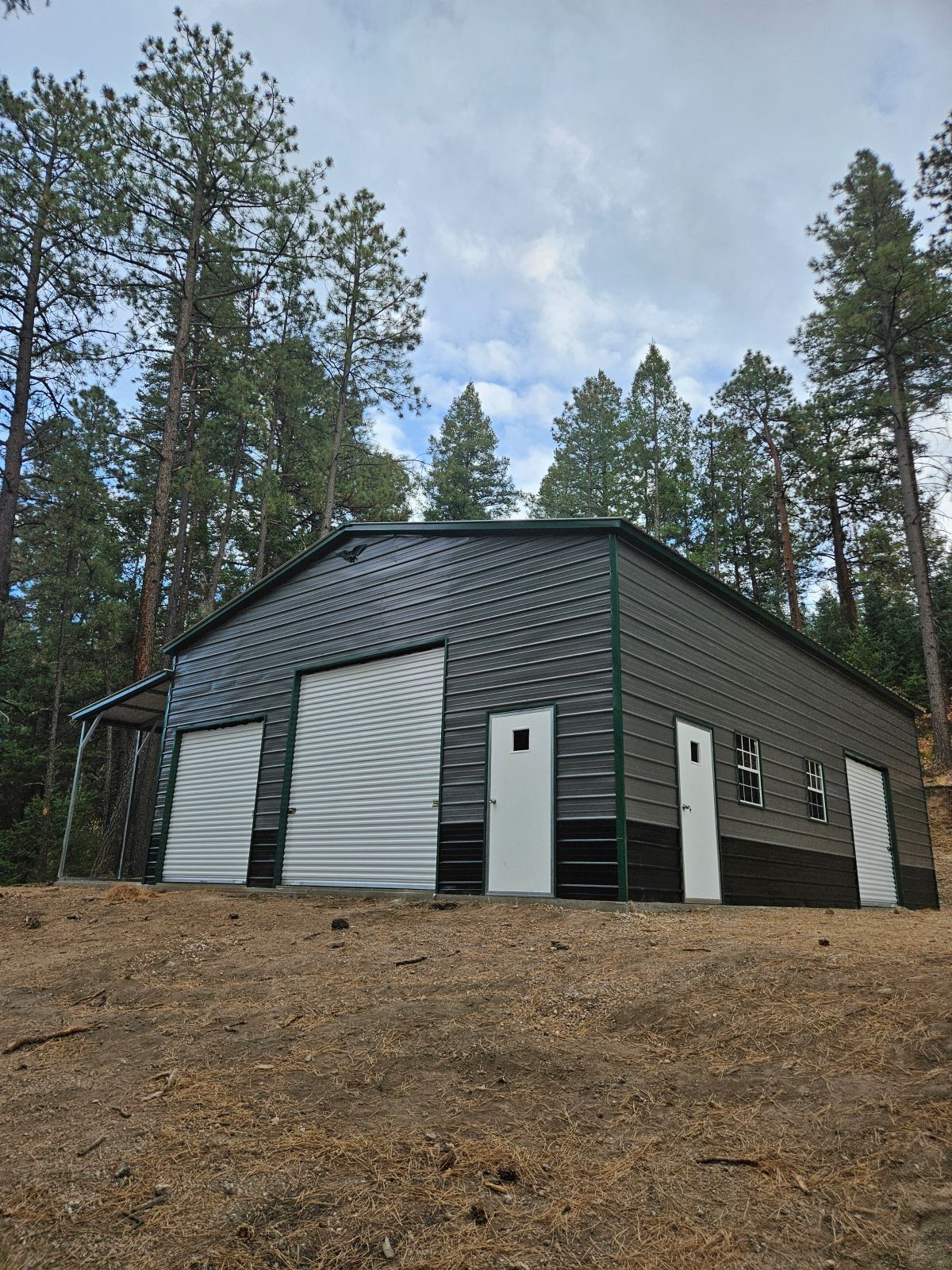 A large metal building is sitting on top of a dirt hill in the middle of a forest.