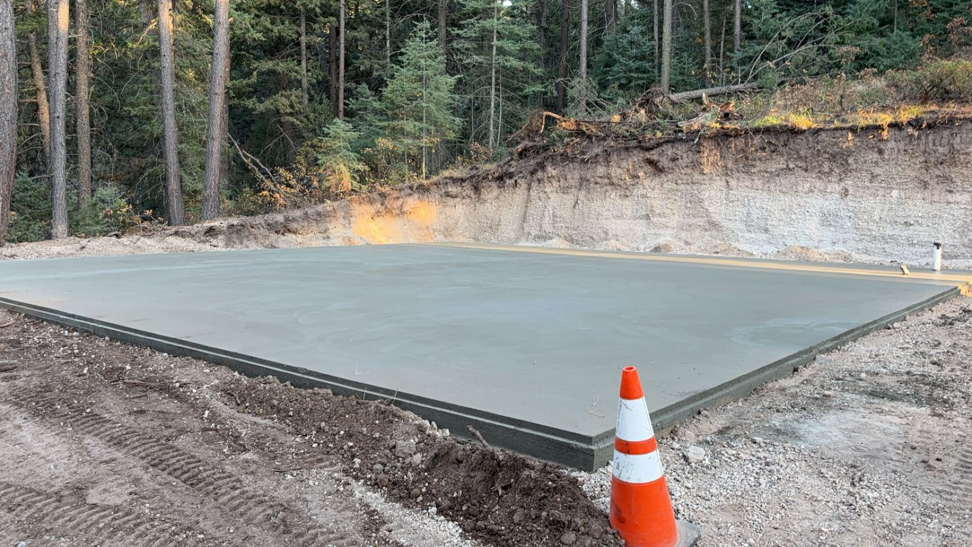A concrete slab is sitting on top of a dirt hill next to a traffic cone.