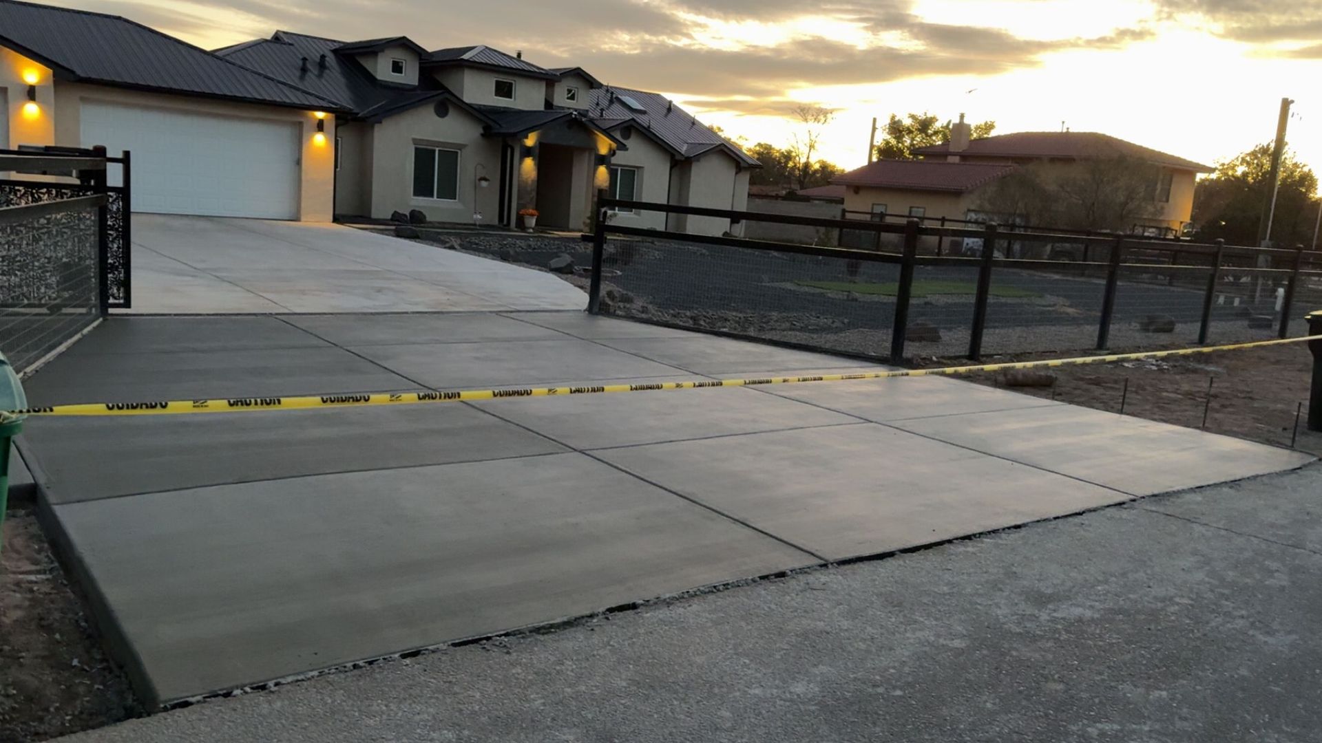 A concrete driveway with a fence and a house in the background.