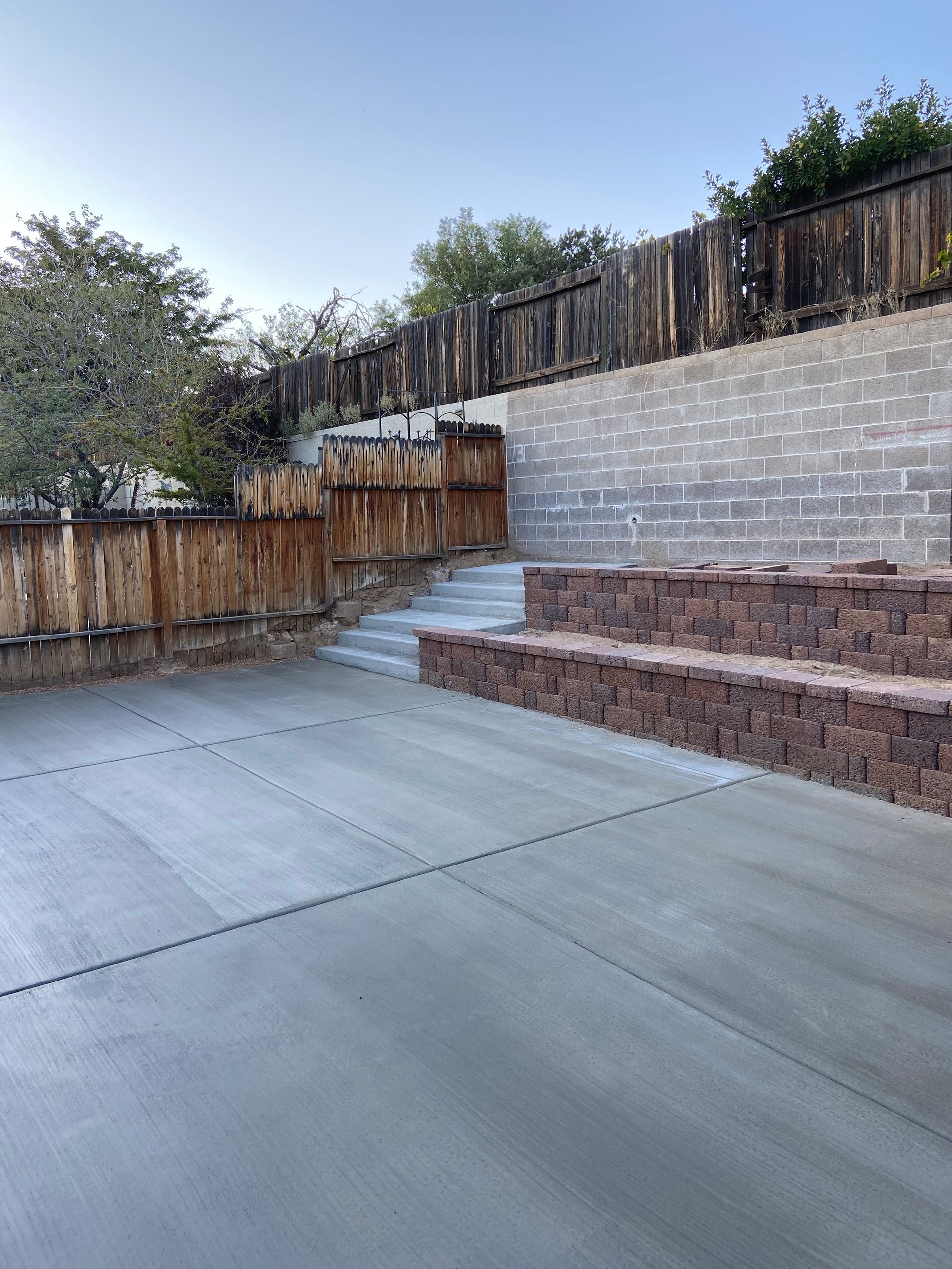 A concrete patio with stairs and a wooden fence in the background.