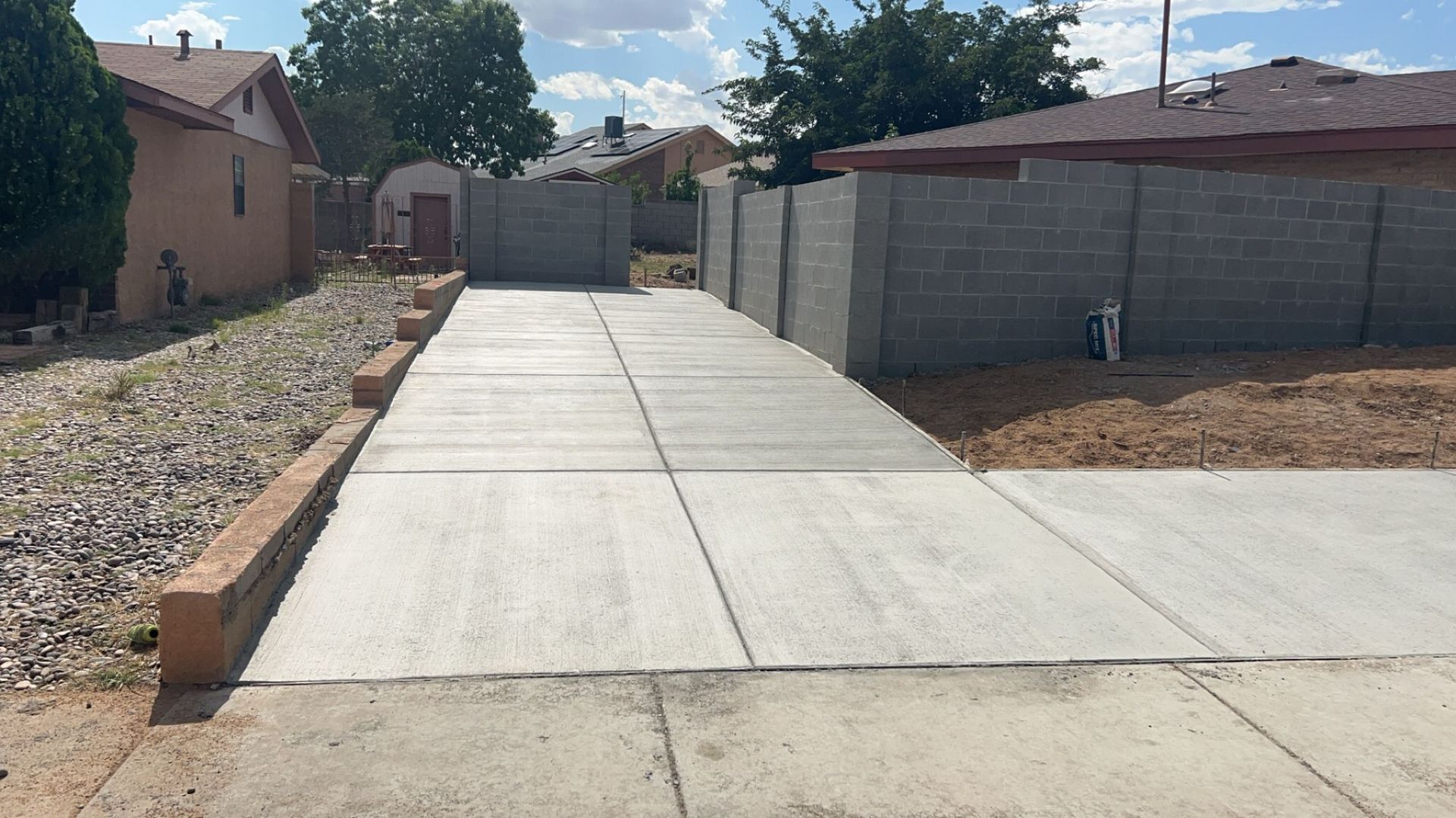 A concrete driveway leading to a house with a fence in the background.