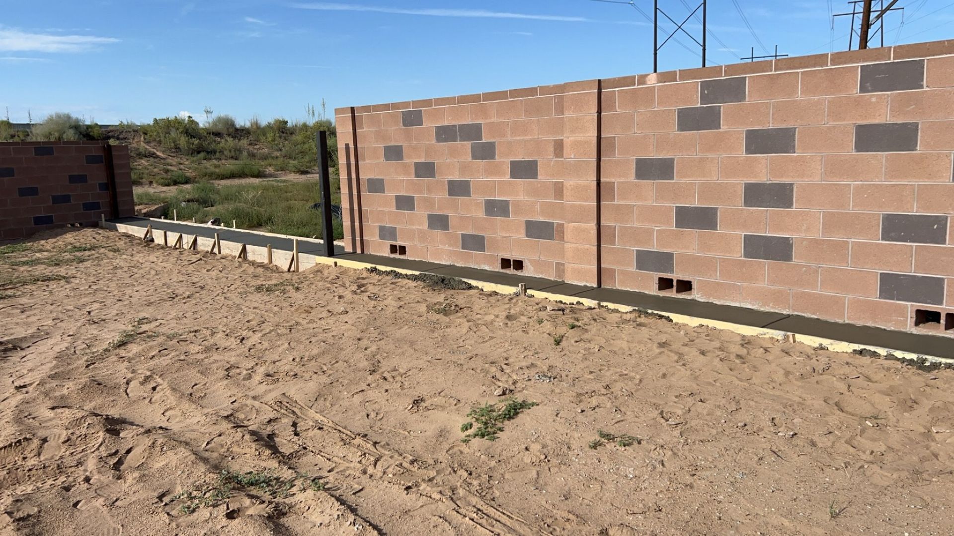 A brick wall is being built in a dirt field.
