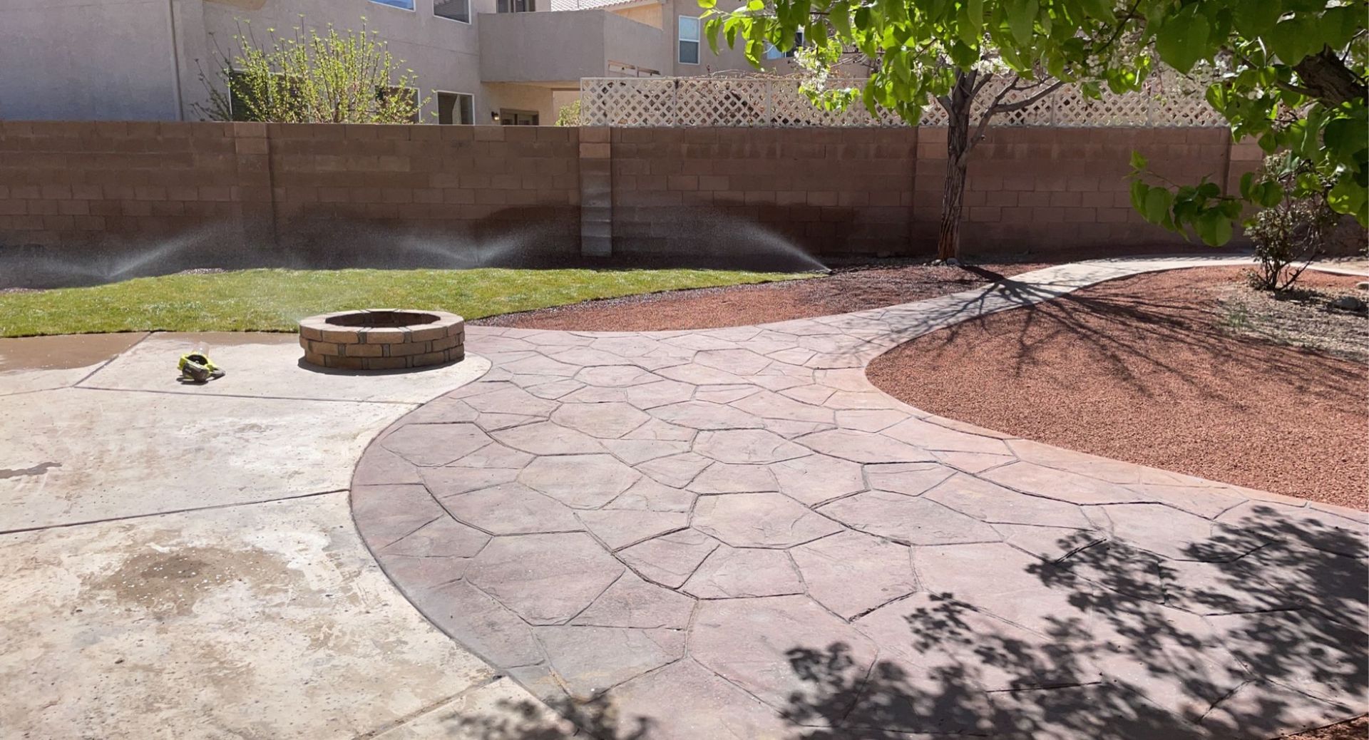 A sprinkler is spraying water on a patio in a backyard.