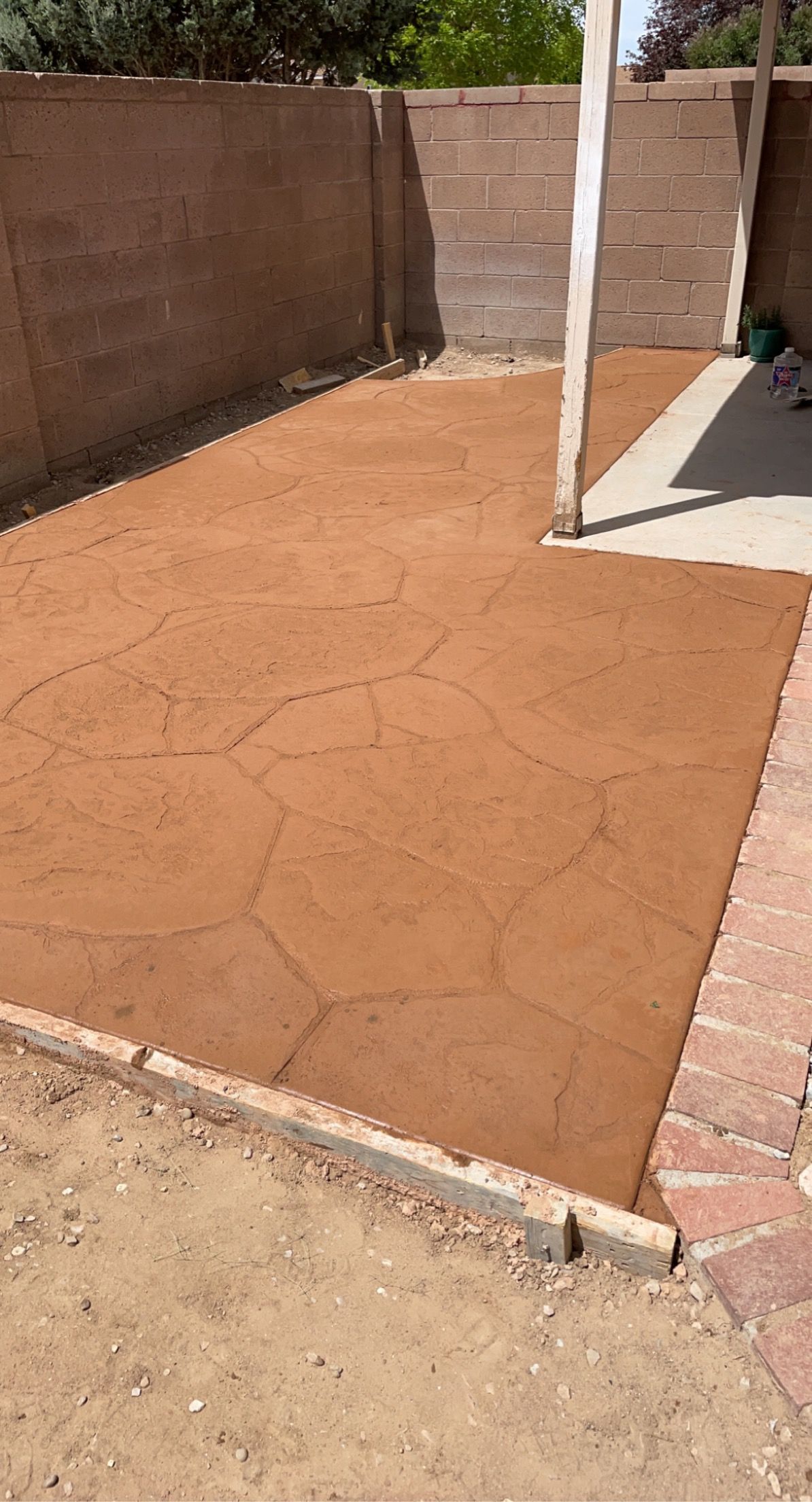 A backyard with a concrete patio and a brick wall.
