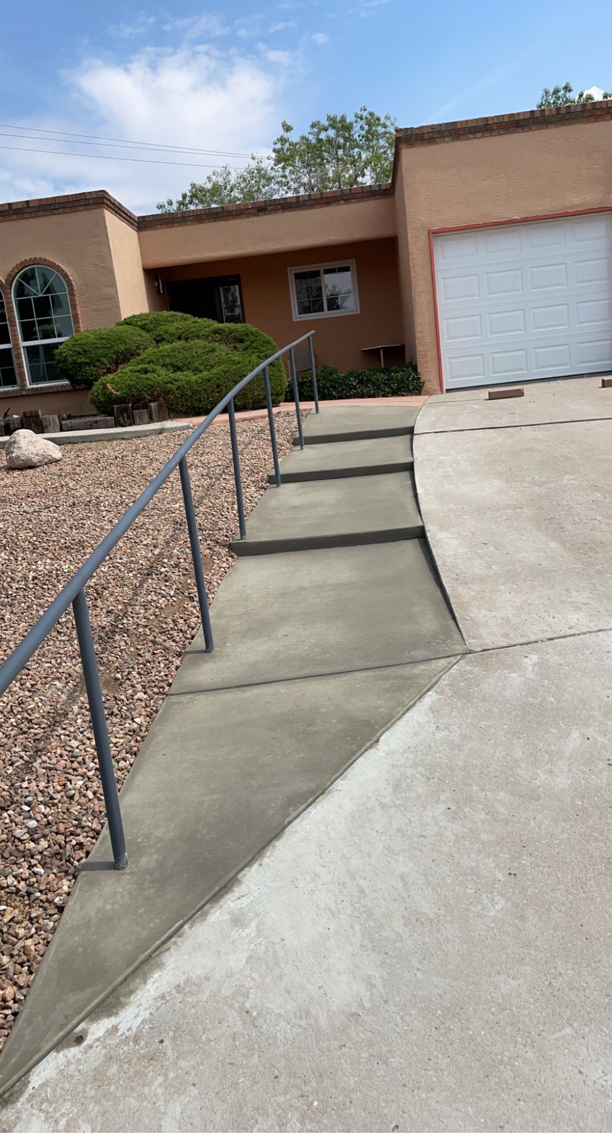 A concrete walkway with stairs and a railing in front of a house.