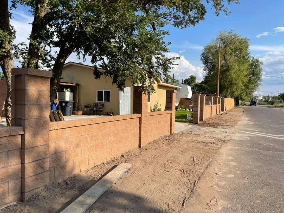 A brick wall along the side of a road with a house in the background