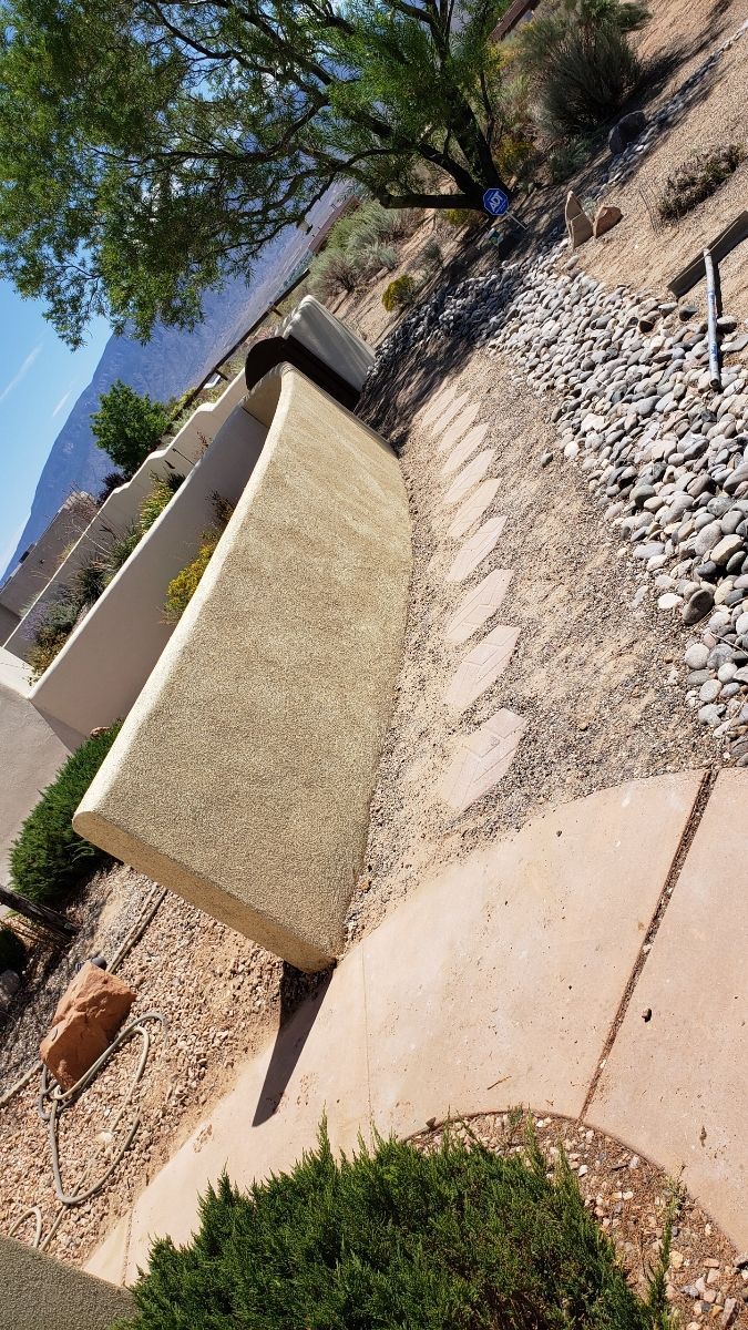 A concrete wall is sitting next to a concrete walkway in a garden.