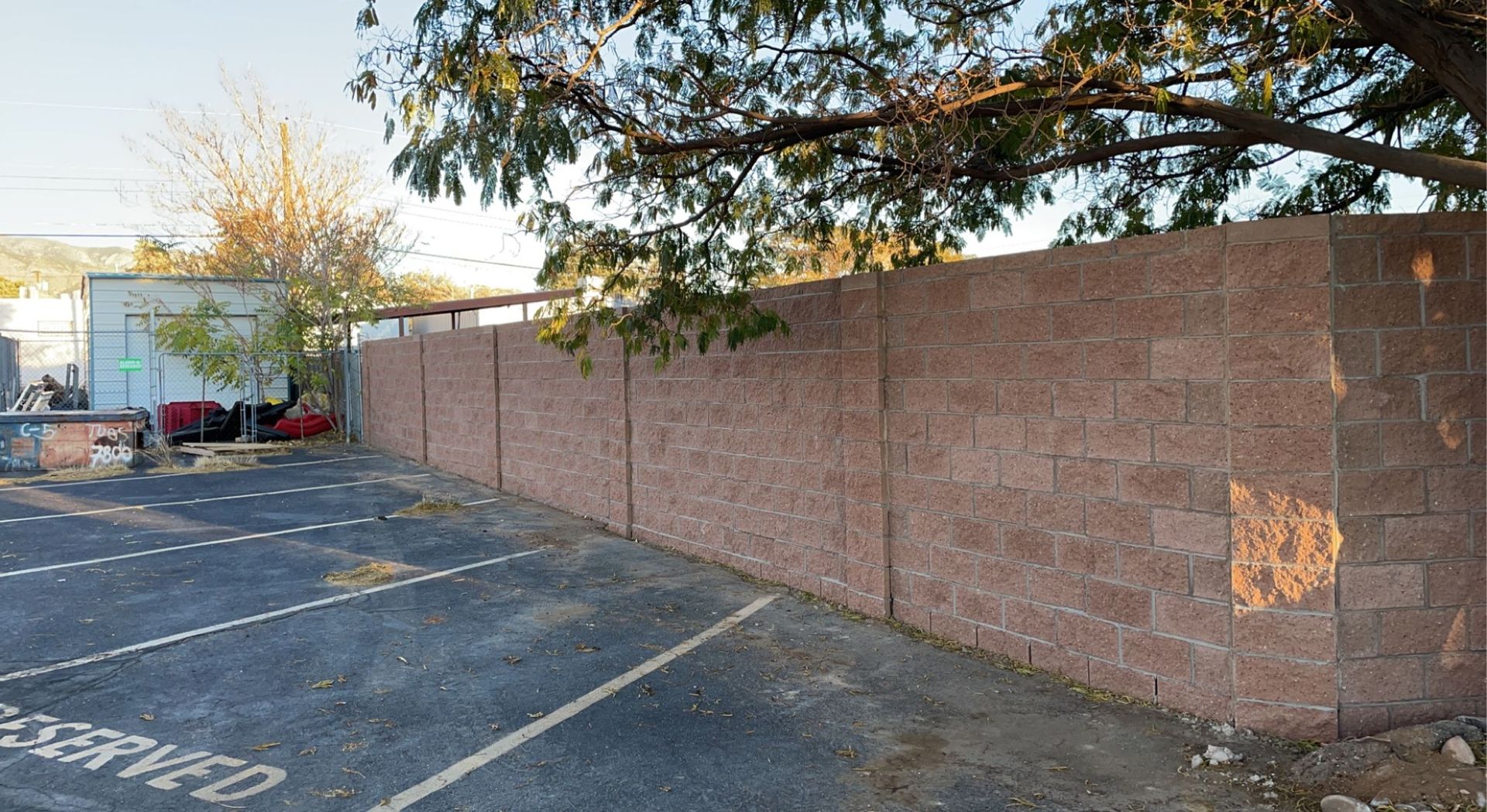 A brick wall surrounds a parking lot with a tree in the background.