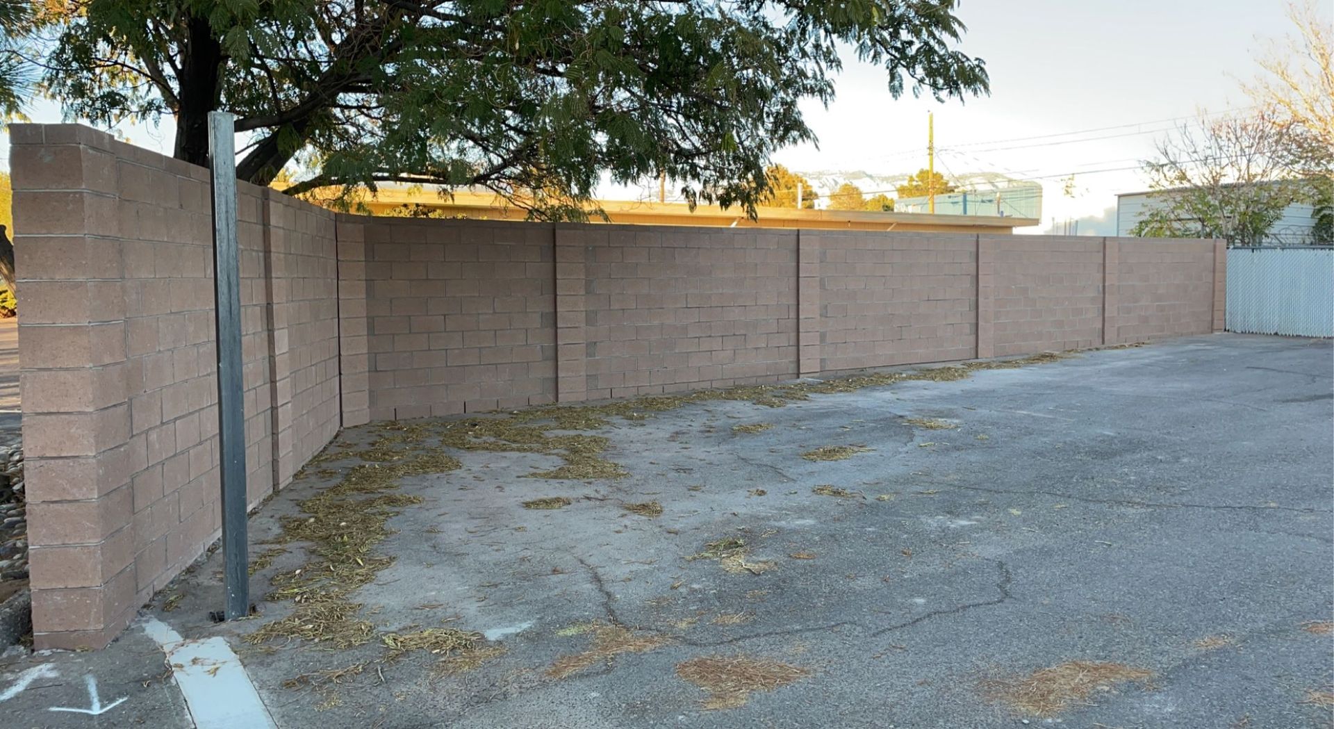 A brick wall surrounds a parking lot with a tree in the background.