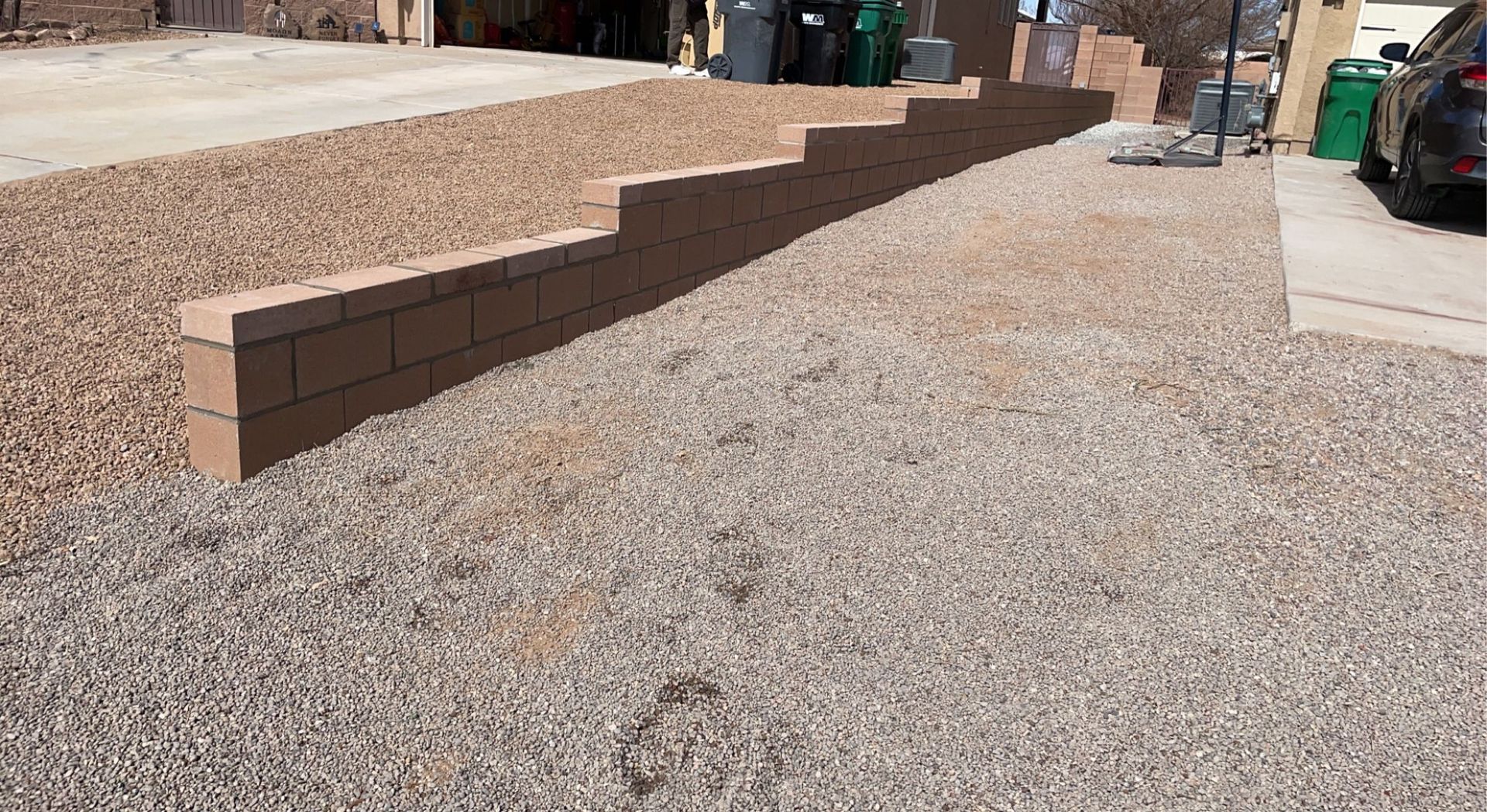 A brick wall is being built next to a gravel driveway.