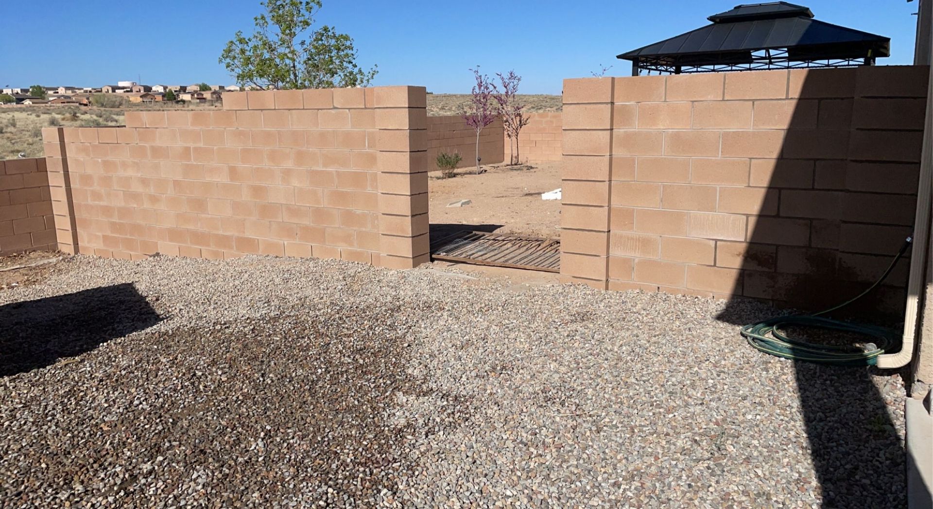 A brick wall with a gazebo in the background and gravel in the foreground.