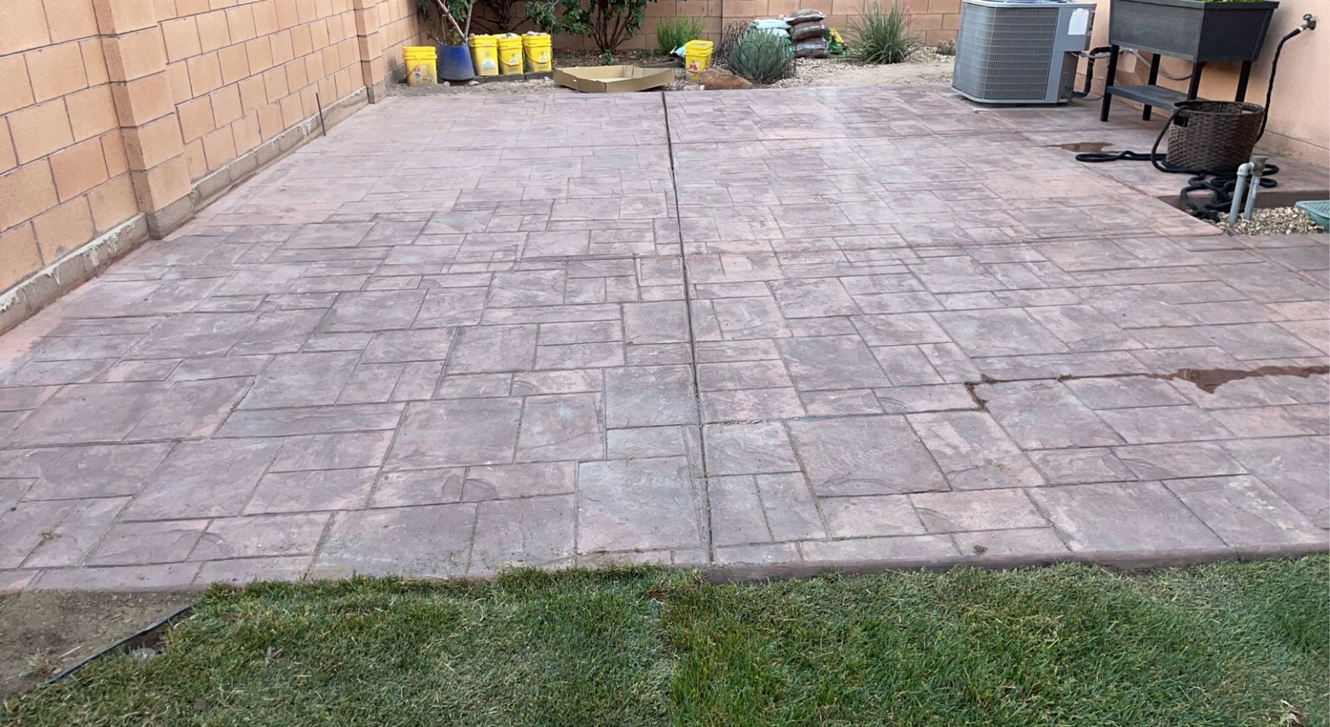 A patio in a backyard with a brick wall and grass.