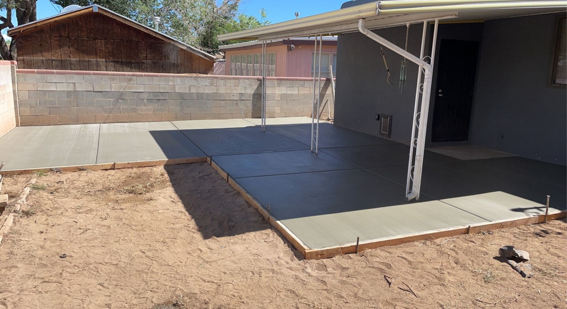 A concrete patio is being built in the backyard of a house.
