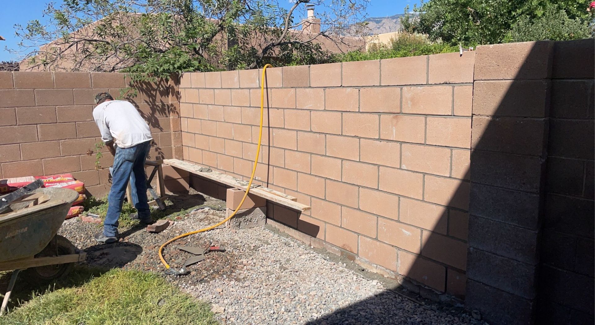A man is working on a brick wall in a backyard.