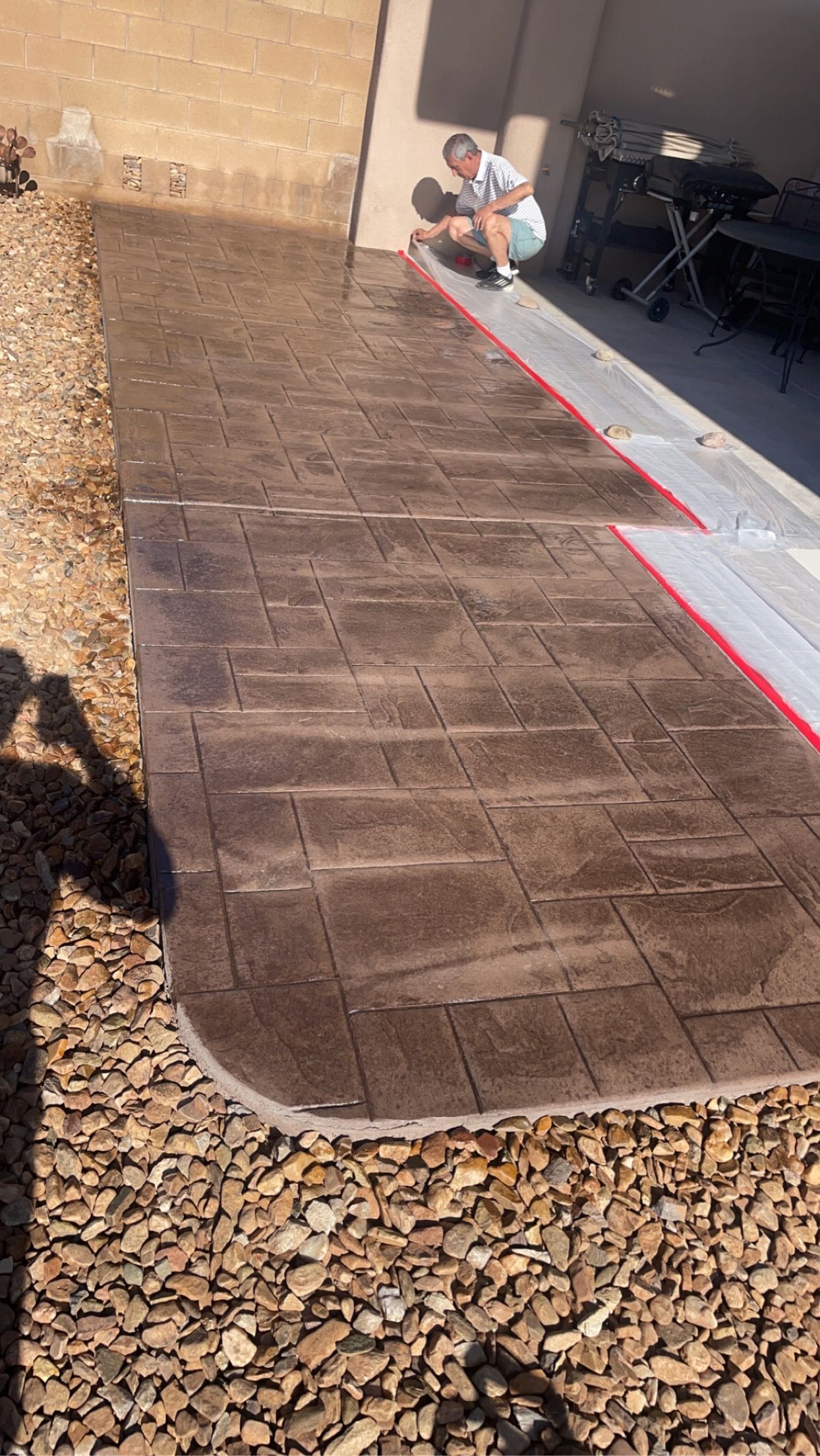 A man is kneeling down on a concrete walkway.