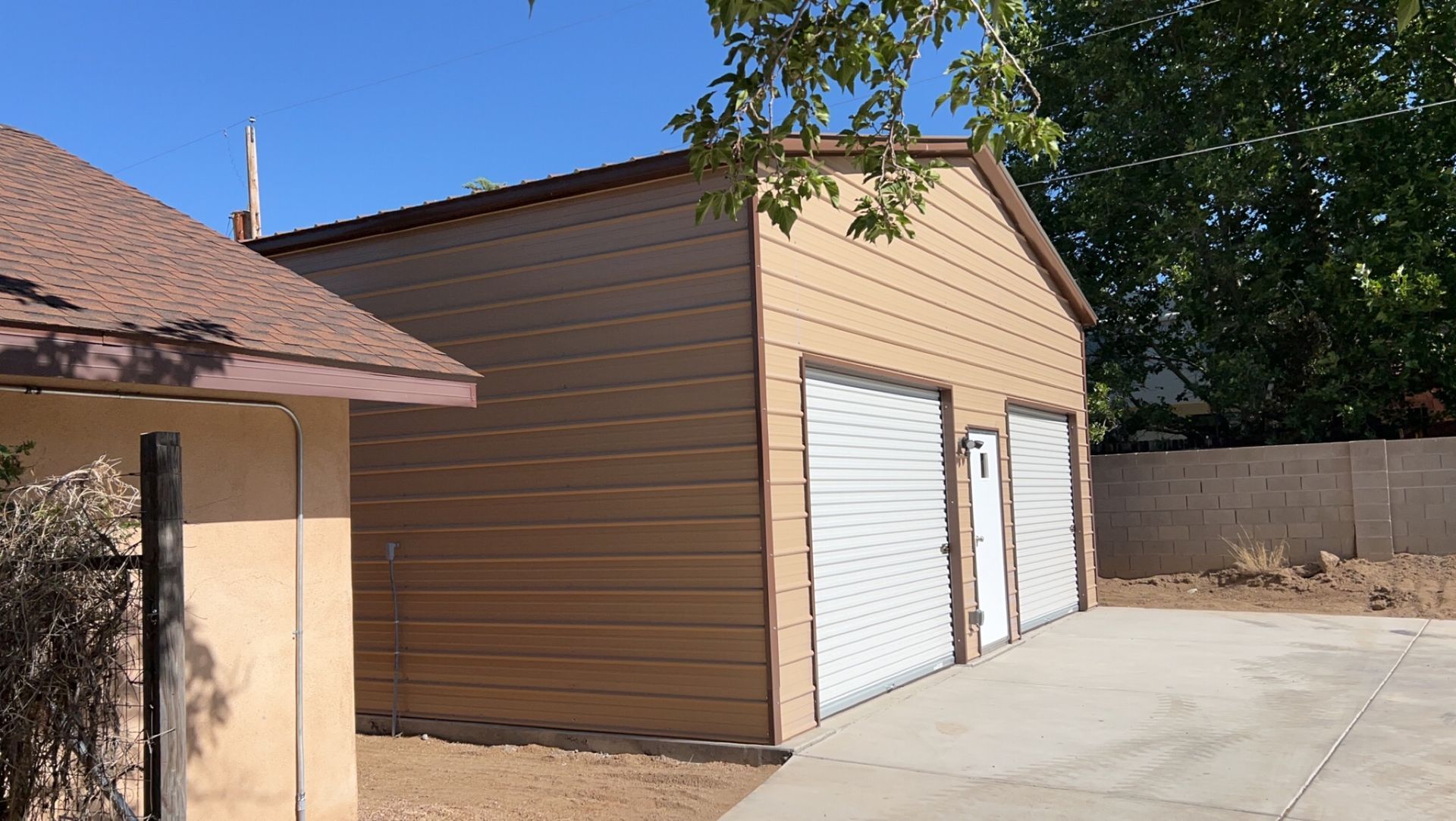 A brown garage with white doors is next to a house.