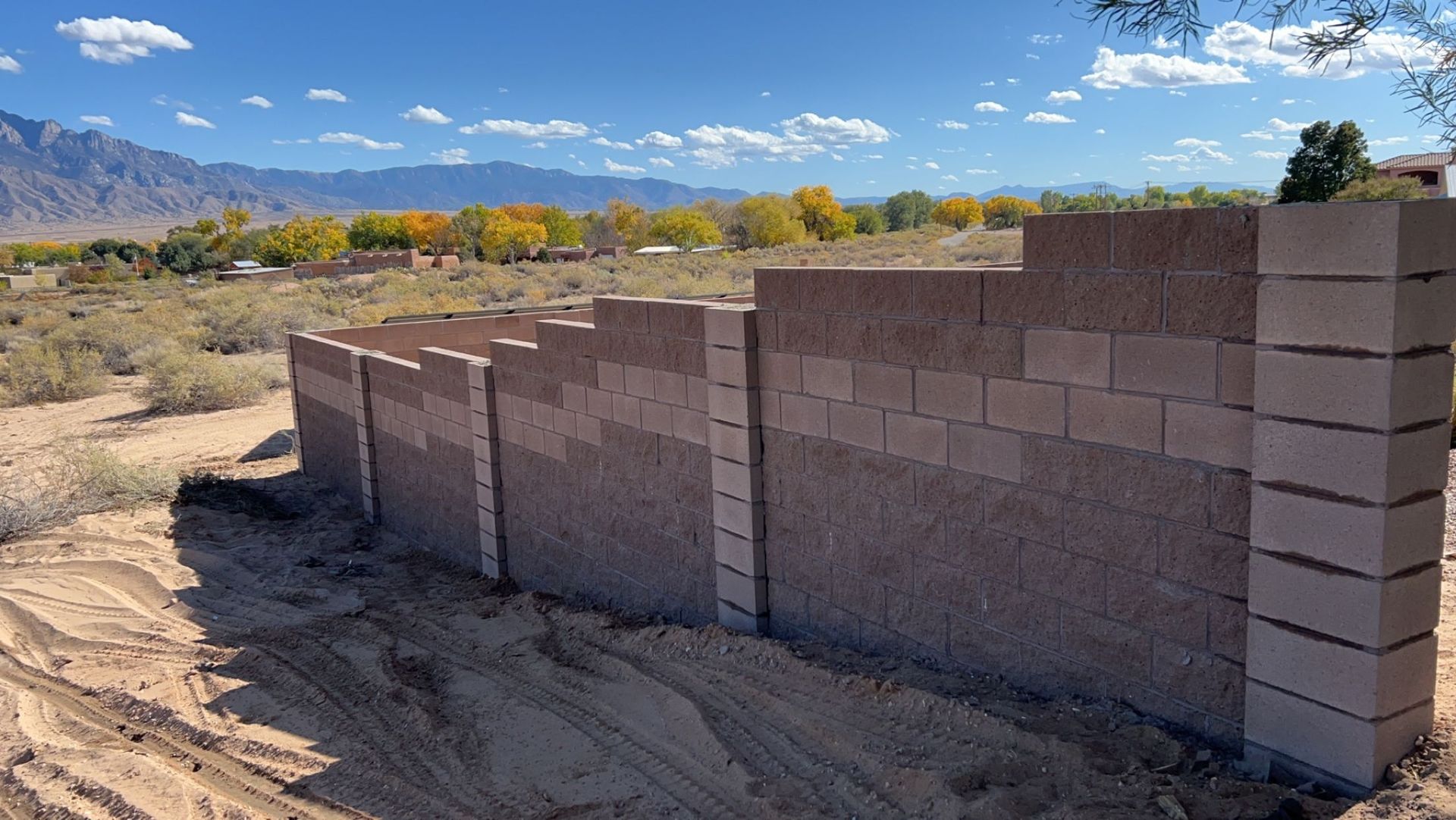 A brick wall is being built in the middle of a dirt field.