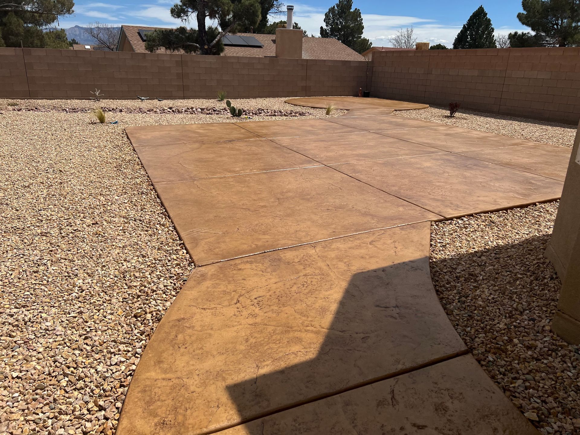 A concrete walkway is surrounded by gravel and a brick wall.