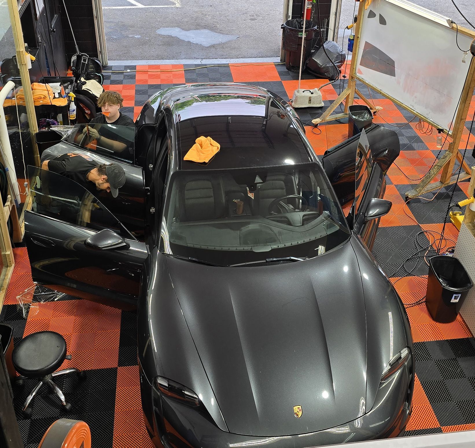 A gray Porsche car with open doors inside a garage, a person inside, black and orange checkered floor.