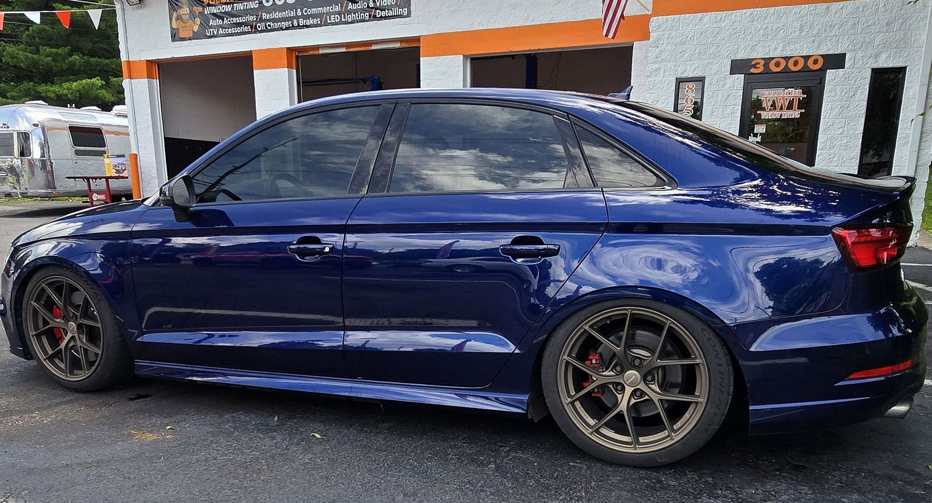 Blue sedan parked outside a business with tinted windows, dark wheels, and red brake calipers.