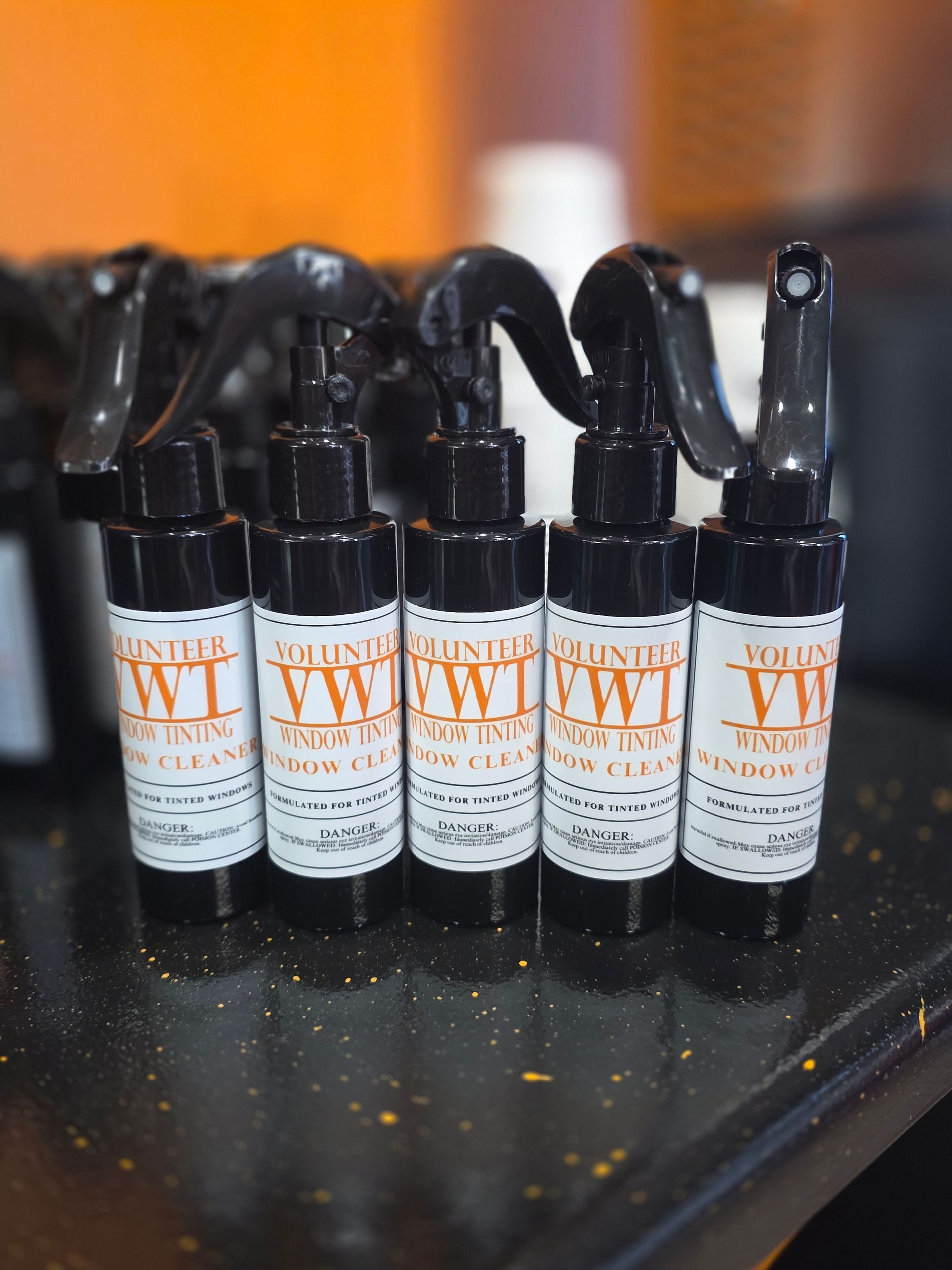 Five black spray bottles with white labels and orange text.