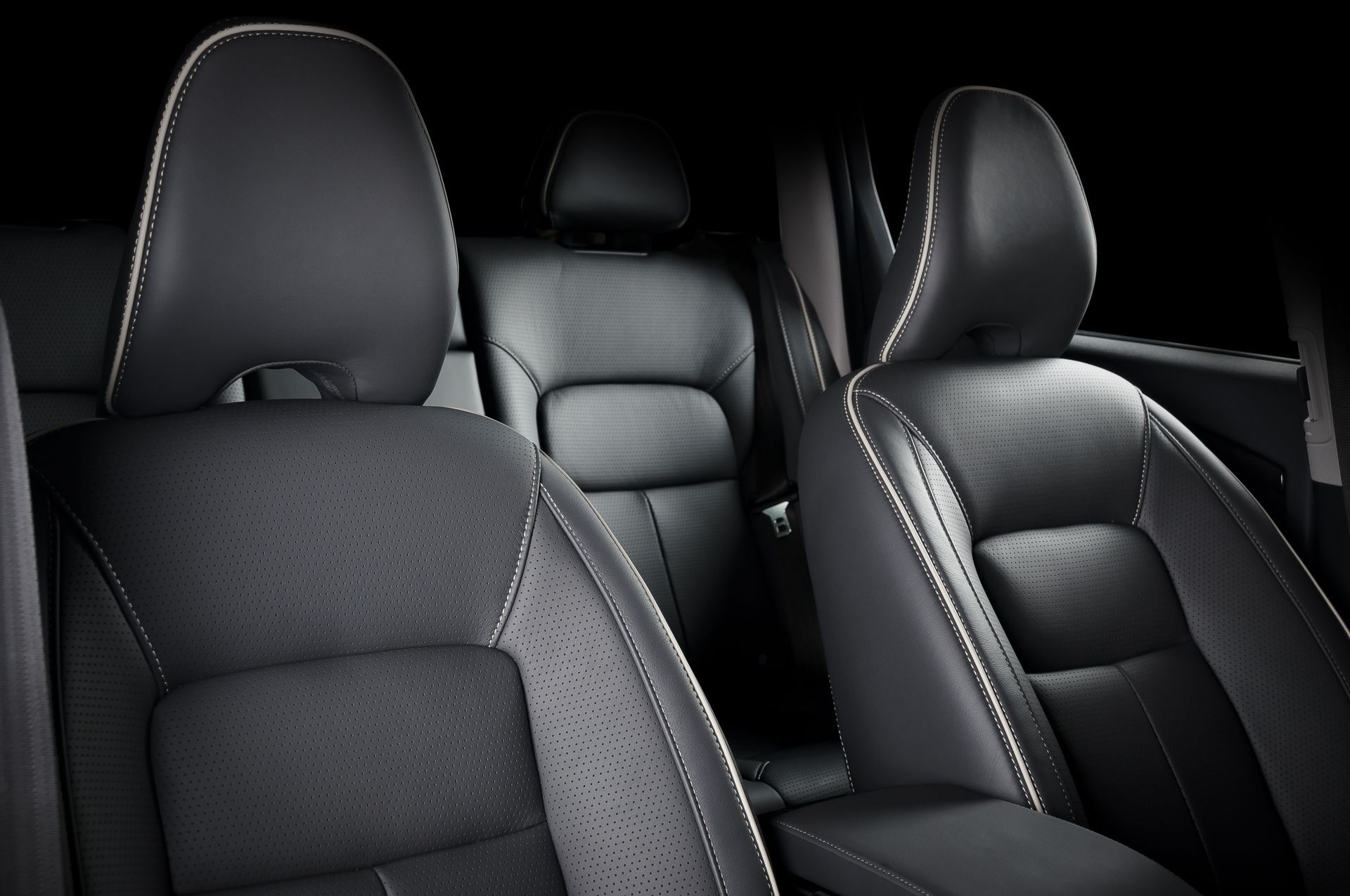 Black leather car seats with white stitching, in a dark interior.