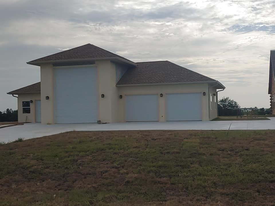 A house with three garage doors is sitting on top of a lush green field.