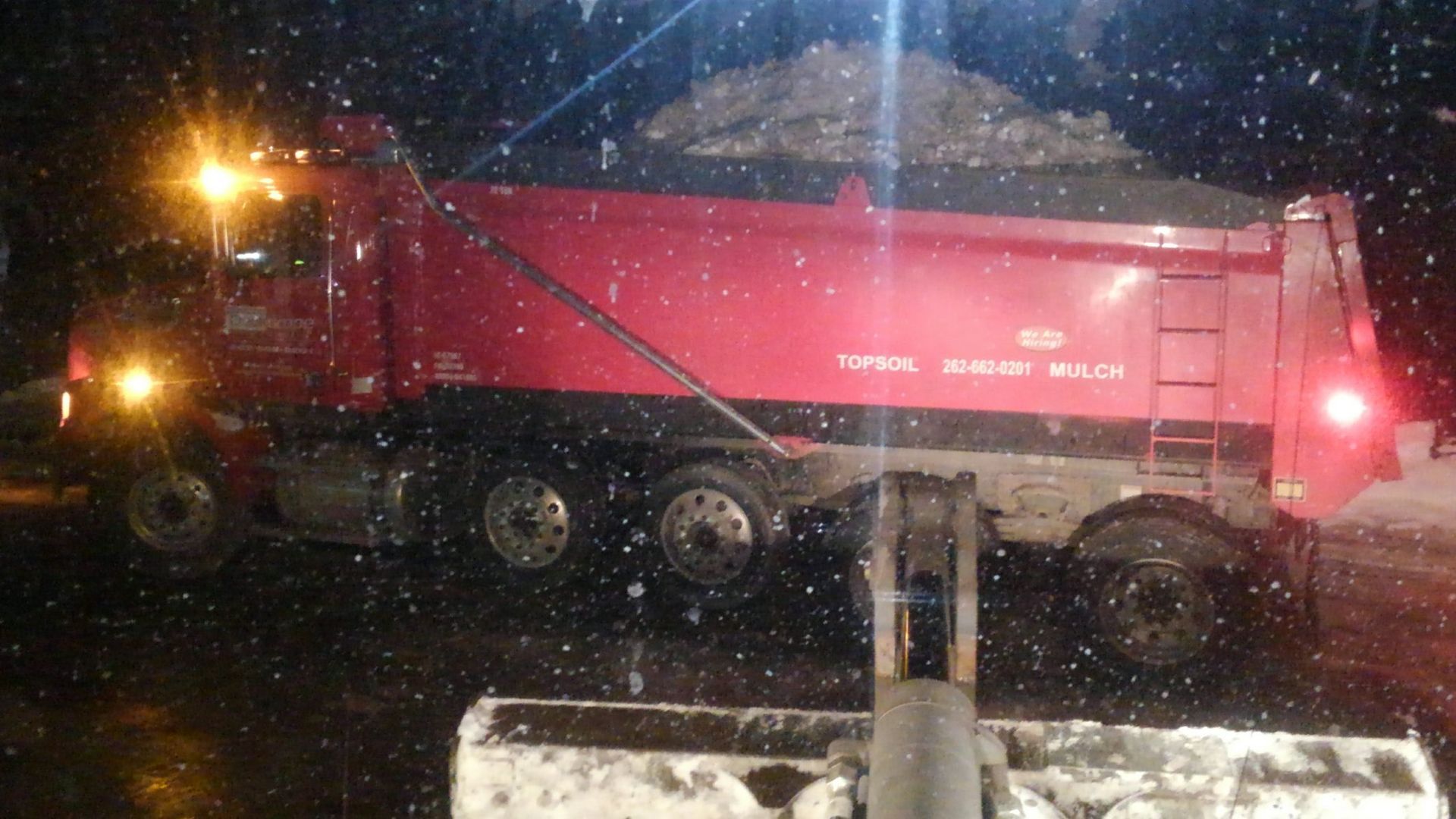 Red snow removal truck at night, loading snow into its bed.