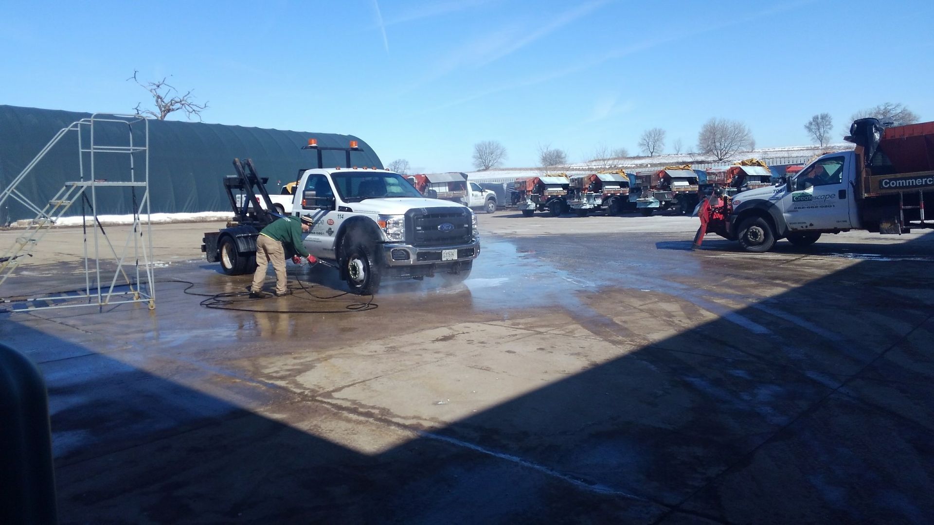 Two white pickup trucks being washed outside, one person working on each.