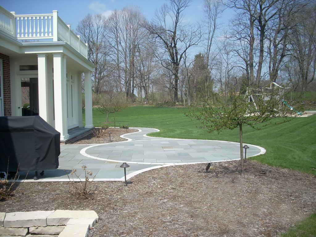 Patio with grey stone, white trim on a house, and a grassy yard.