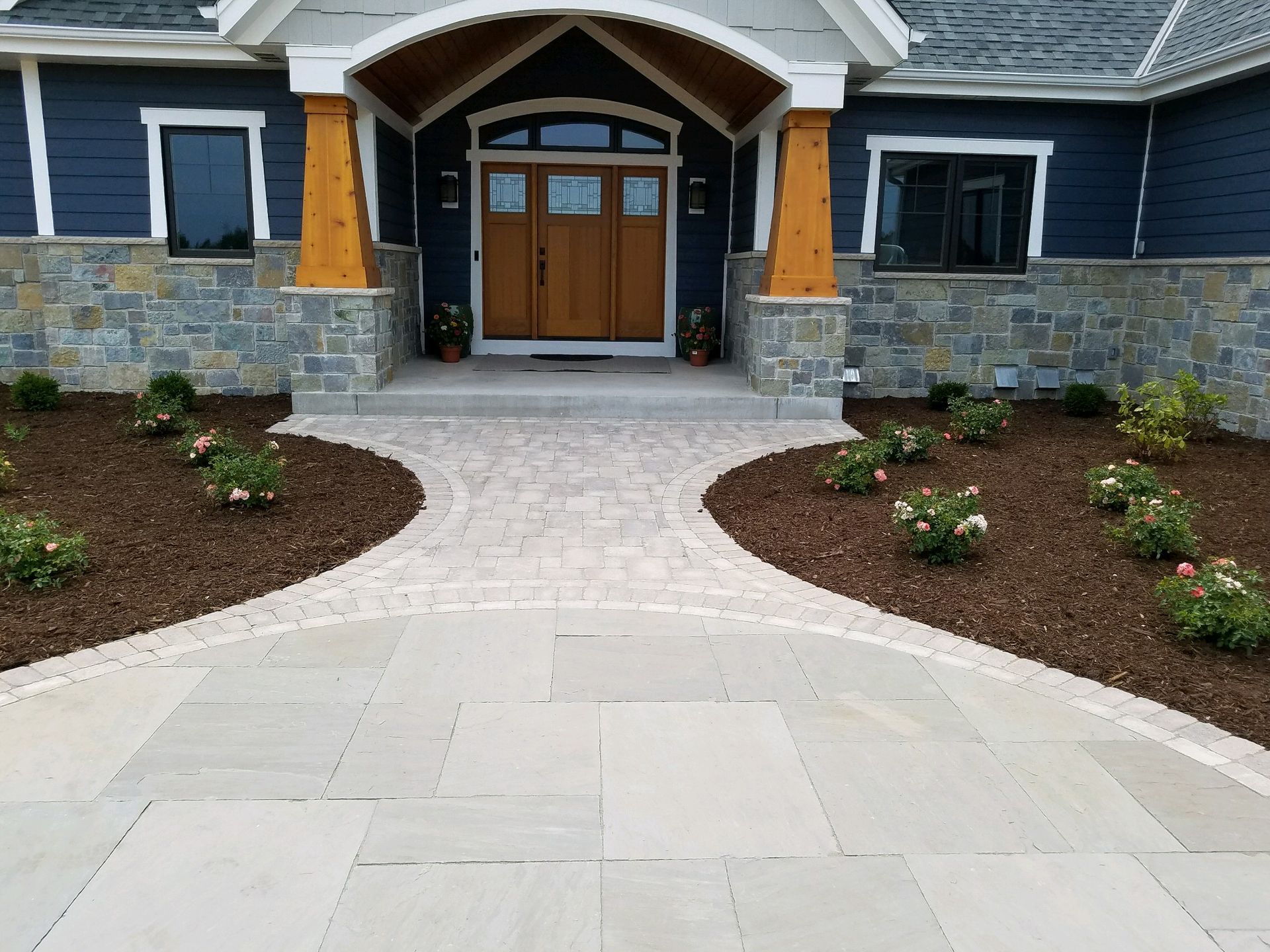 A stone walkway leads to a blue house with wood accents and a covered entryway.