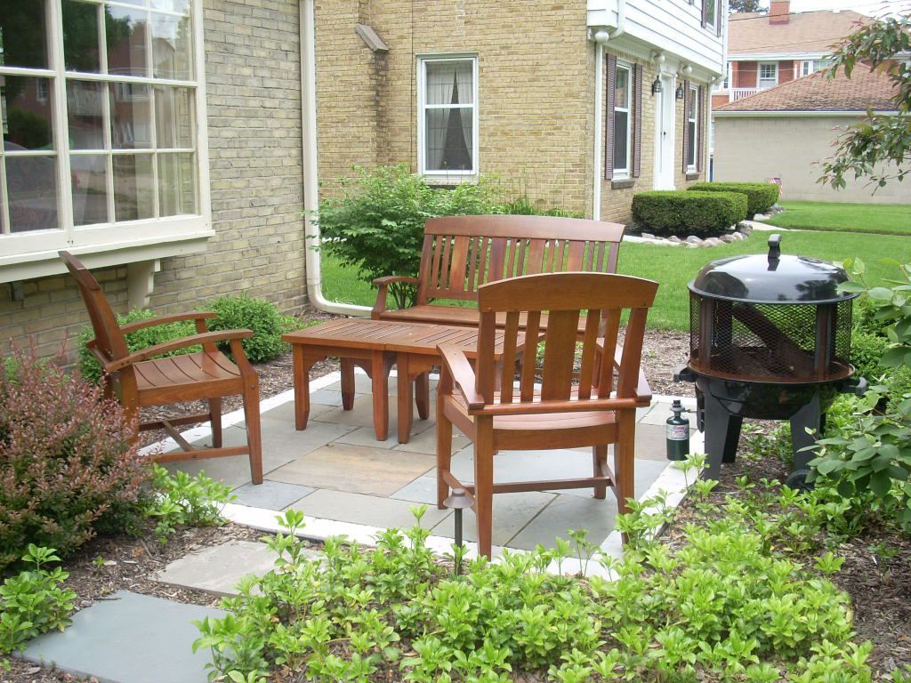 Outdoor patio with wooden furniture, fire pit, and stone pavers near a house.