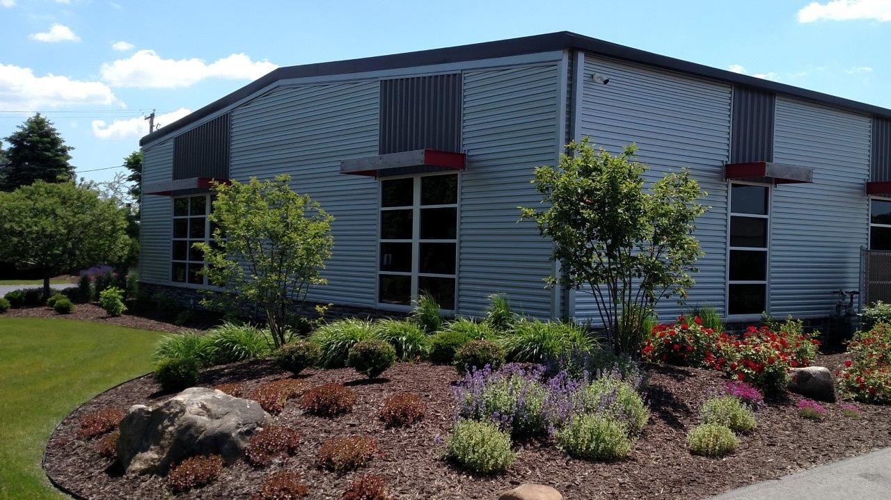 Metal-sided building with several windows, landscaping, and a blue sky.