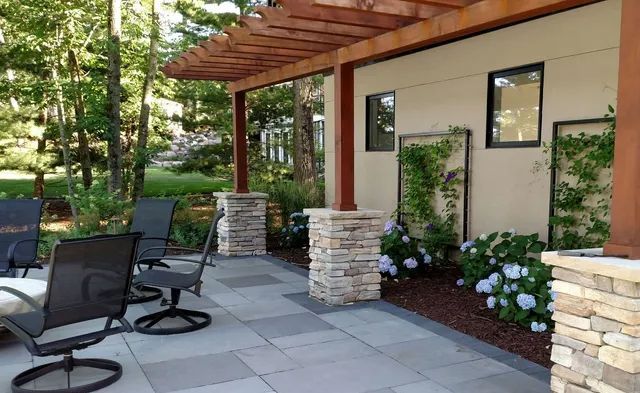 Patio with seating, stone pillars, pergola, and climbing plants on a light-colored building.